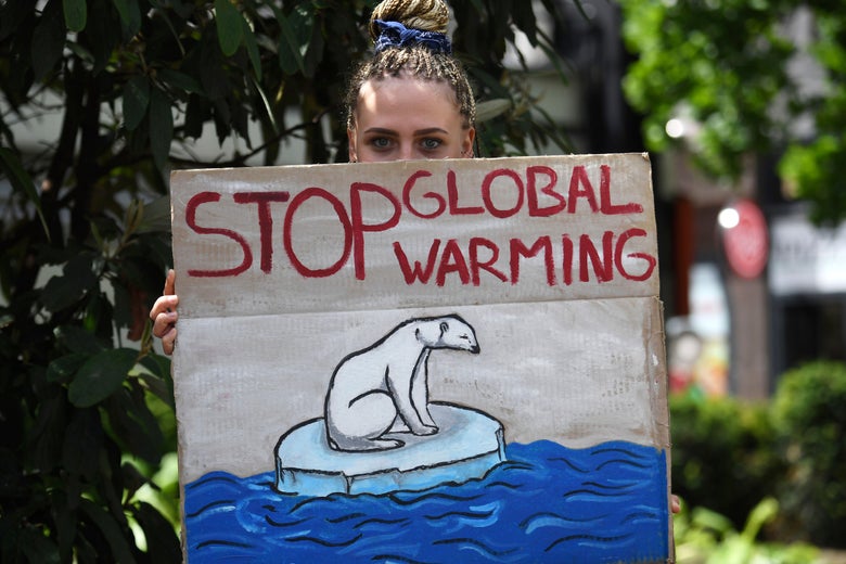 A young woman holds a sign that says "Stop Global Warming" with a polar bear on ice in the middle of water.