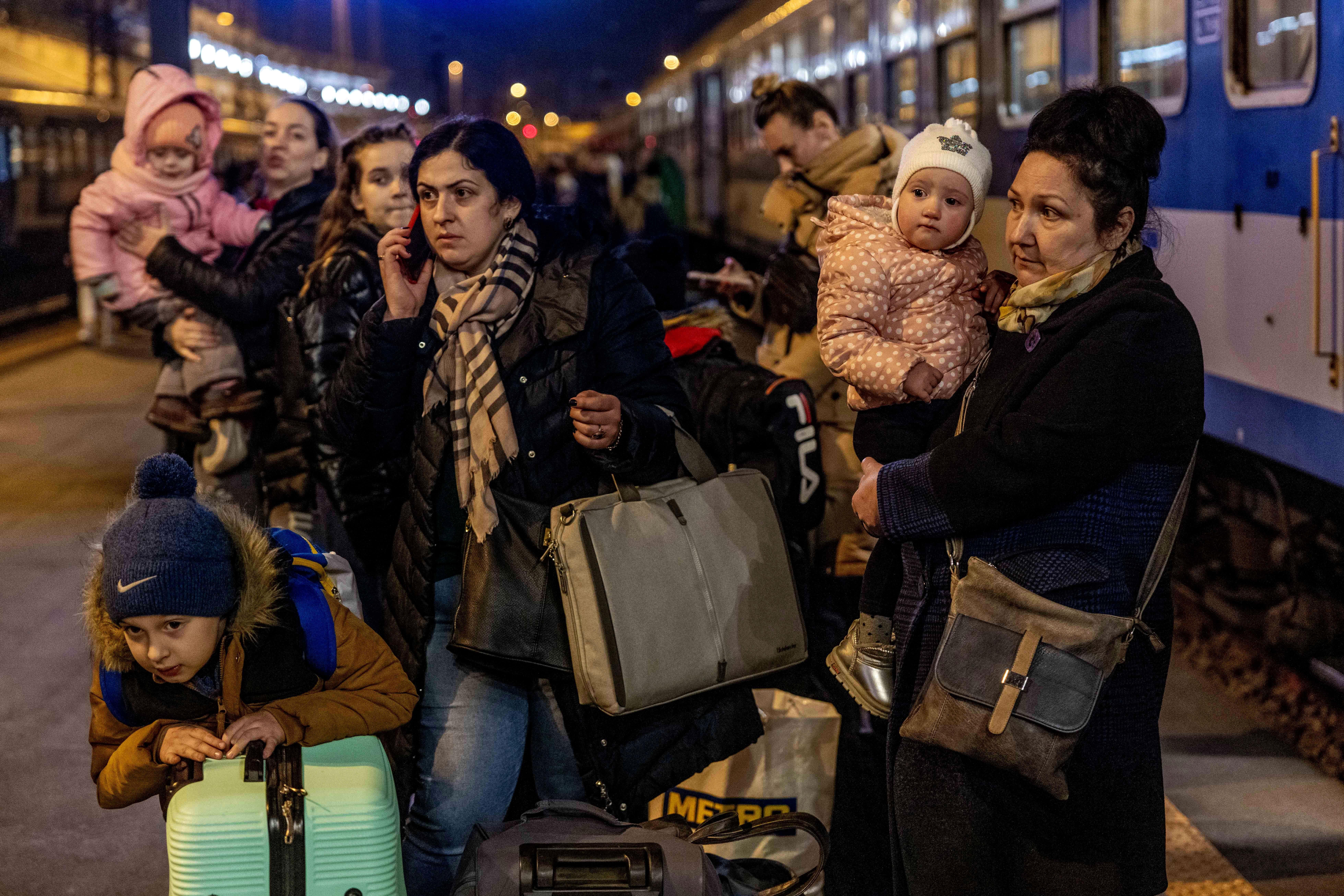 A group of people with kids and luggage walk on a train platform at night