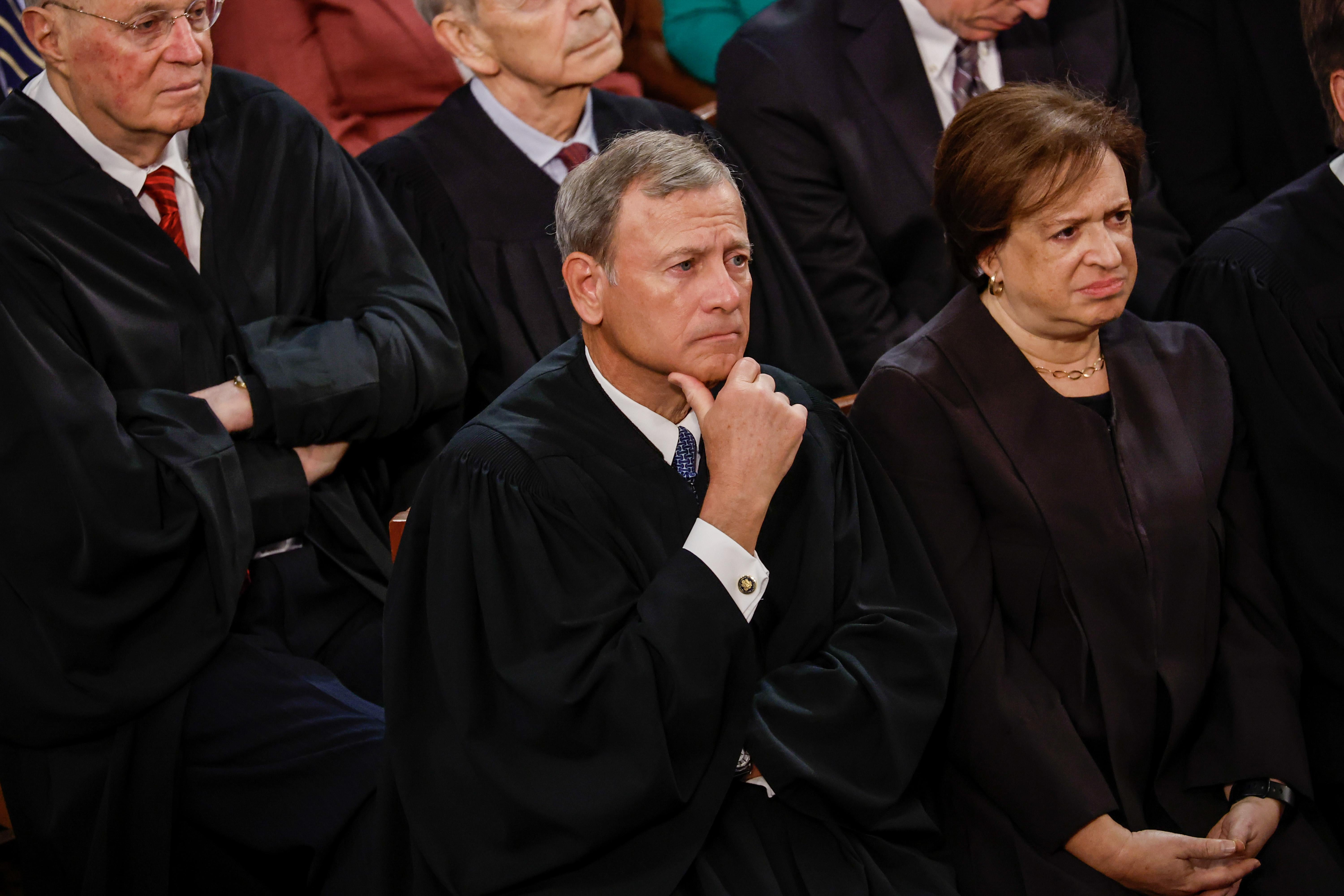 Roberts puts his hand on his chin like he's listening carefully, Kagan clasps her hand like she's doing the same.