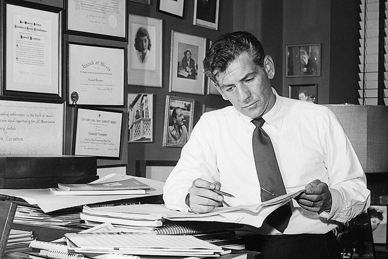 Leonard Bernstein, wearing a shirt and tie, sits in his office and examines some sheets.