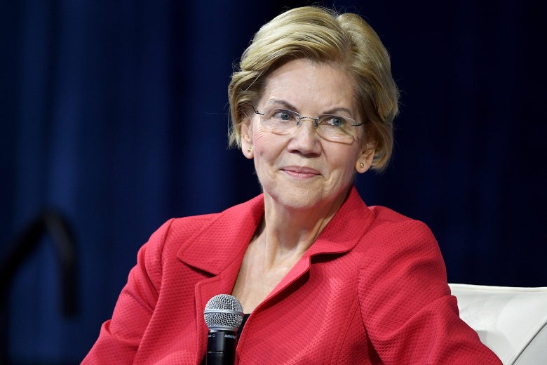 Warren seated onstage, holding a mic.
