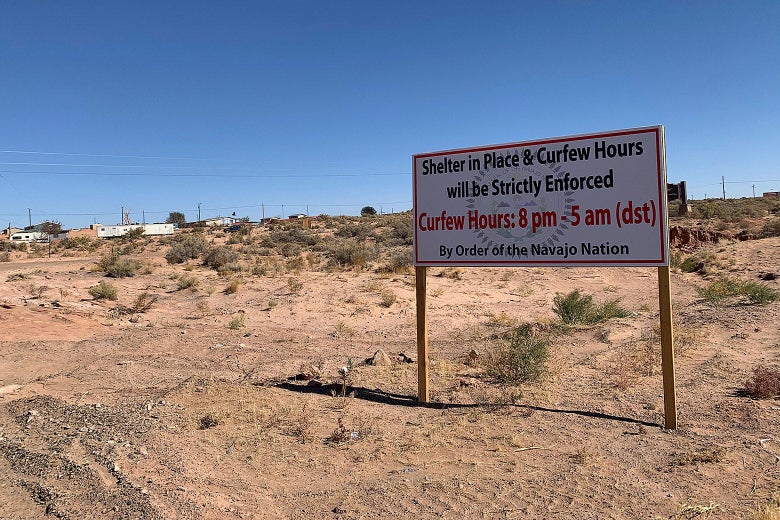 A sign standing in a dry landscape that says "Shelter in Place and Curfew Hours Will Be Strictly Enforced. Curfew Hours: 8 p.m. to 5 a.m. DST by Order of the Navajo Nation"