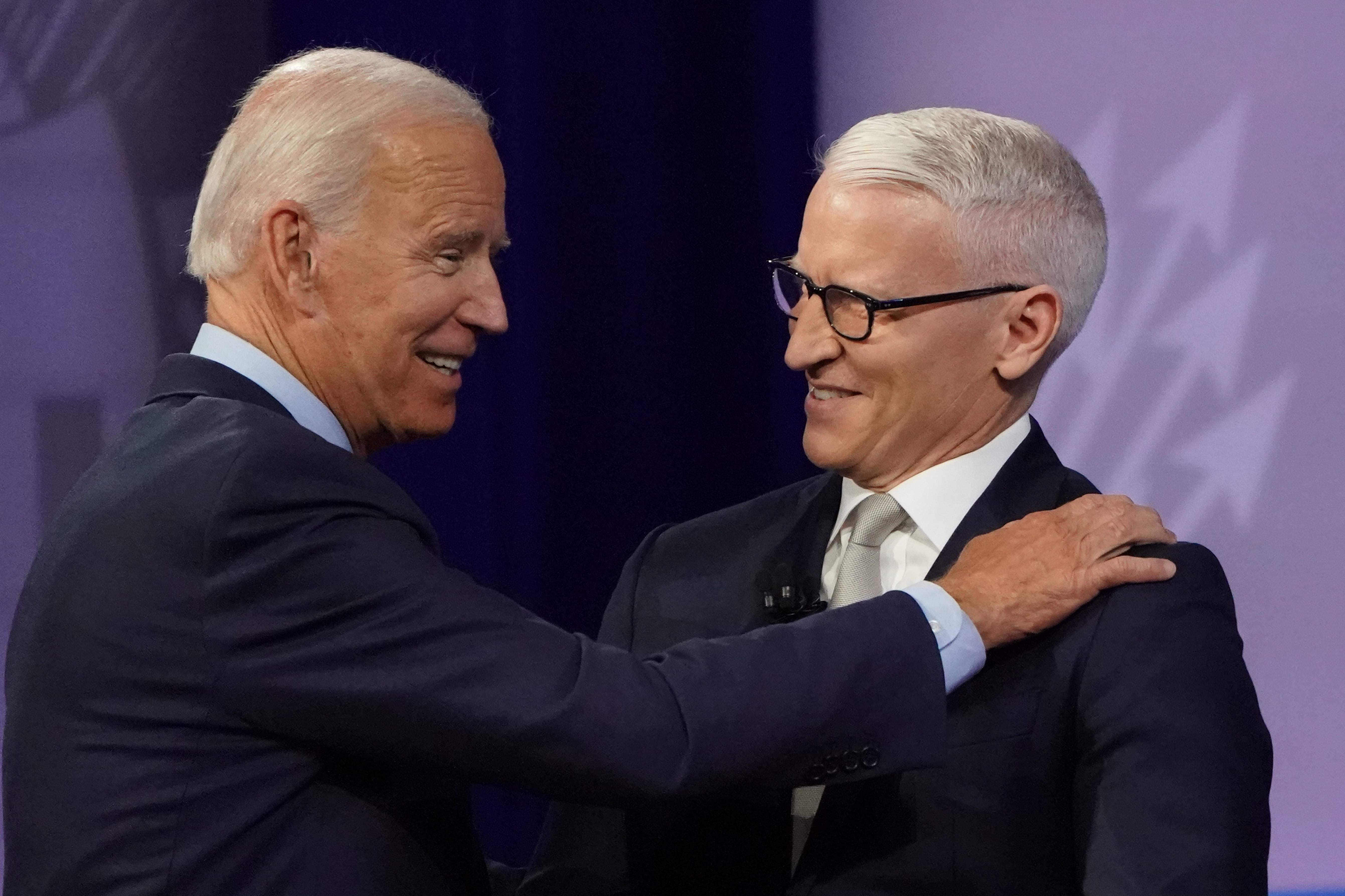 Joe Biden places his right hand on Anderson Cooper's right shoulder as both men smile.
