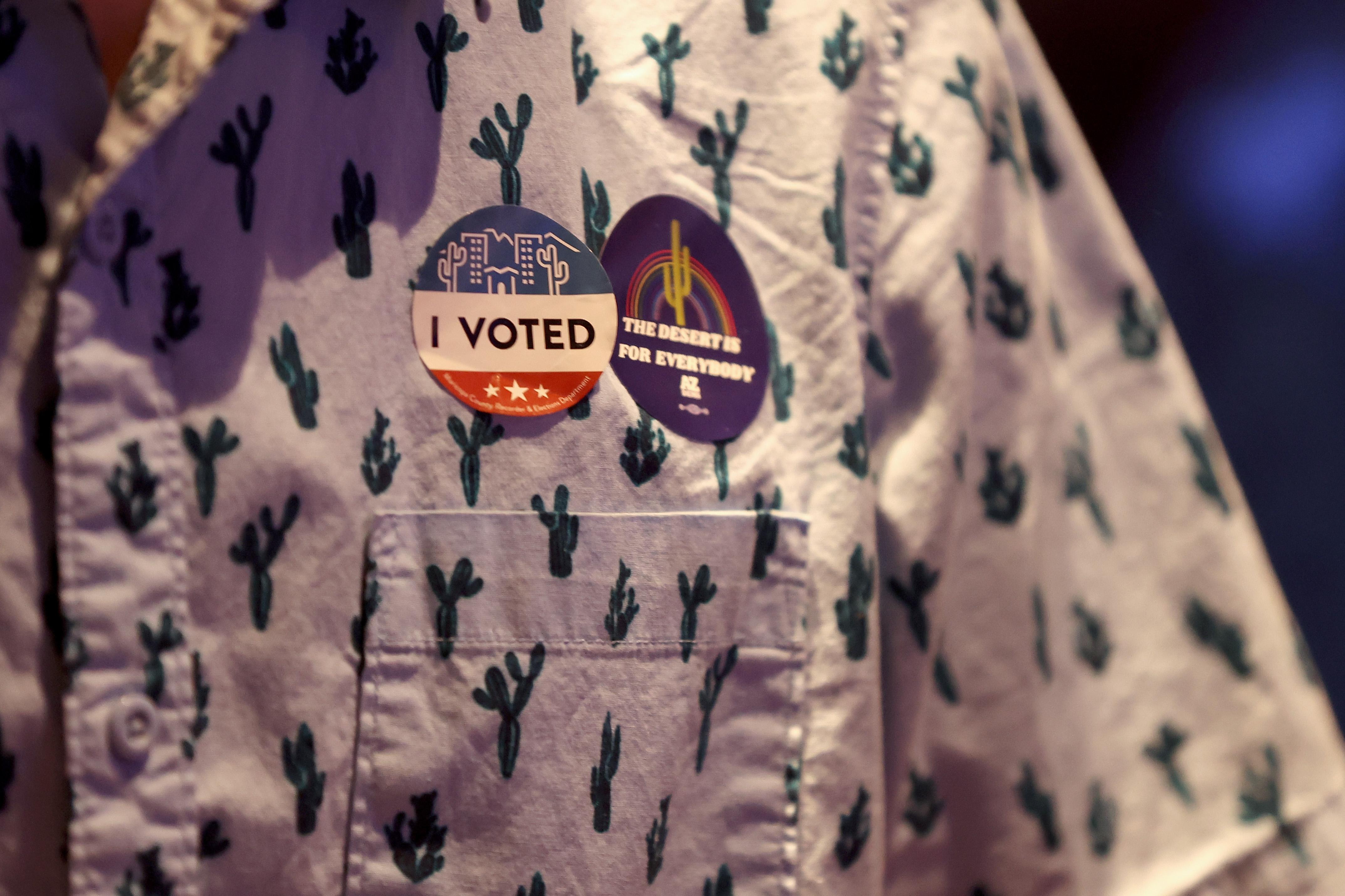 A close-up of a cactus shirt, an "I Voted sticker, and a sticker that says "The Desert Is for Everybody."