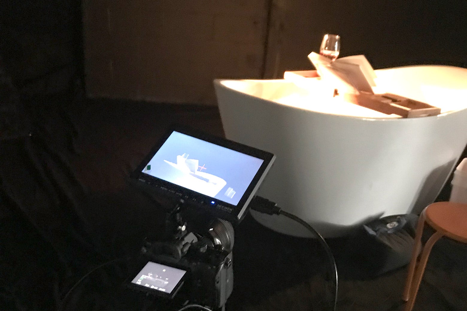 A camera pointed toward a bathtub with a book and a glass of wine on a tray over the tub.