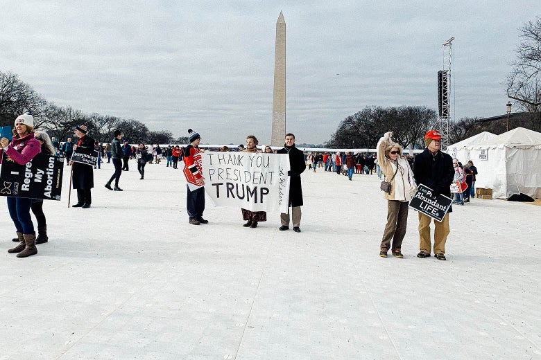 A woman and two young men hold a sing that says "Thank you President Trump" on an expanse of white flooring on the National Mall. The Washington monument is in the background.