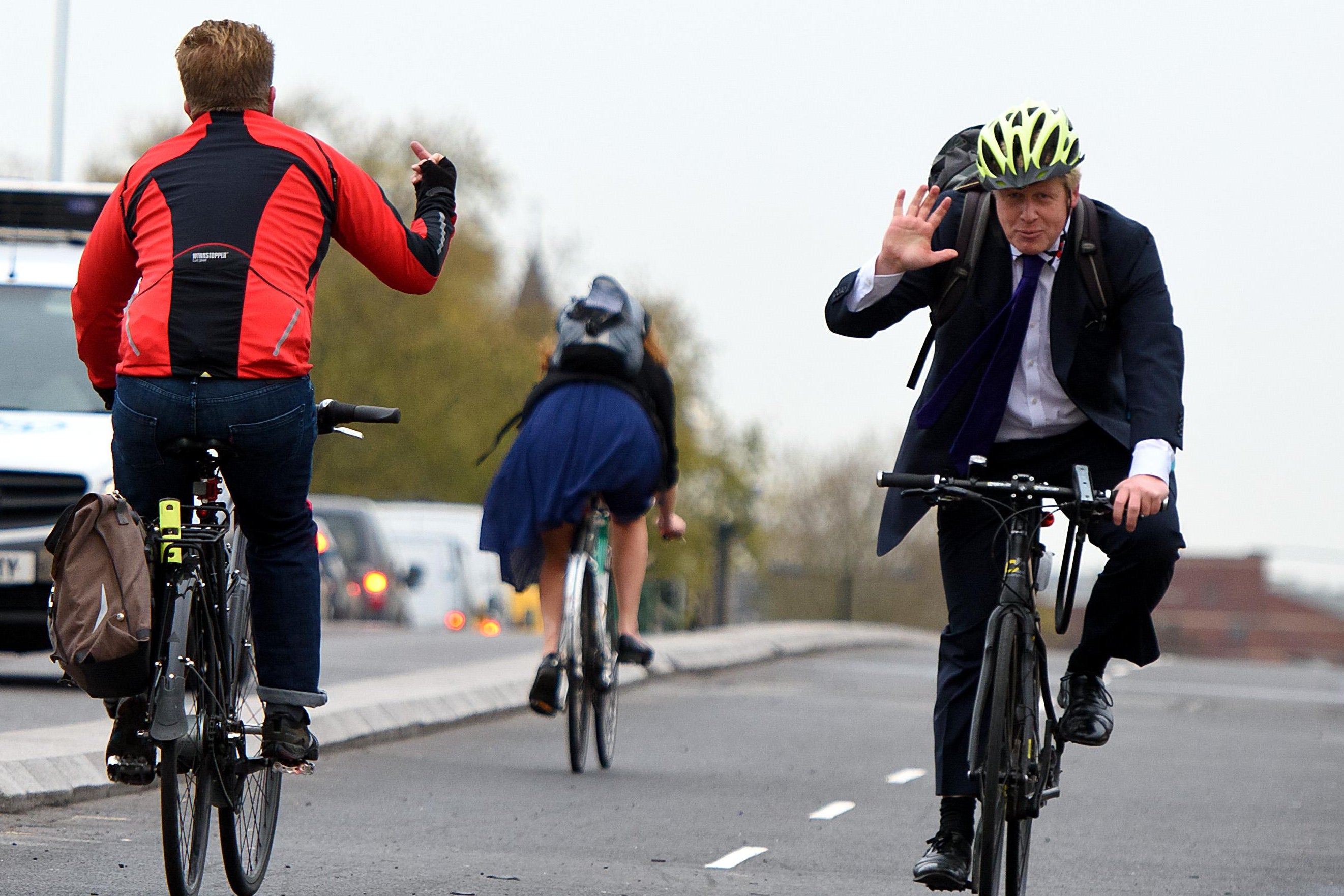 A biker (L) flips off Boris Johnson (R) as he waves and approaches on a bike.