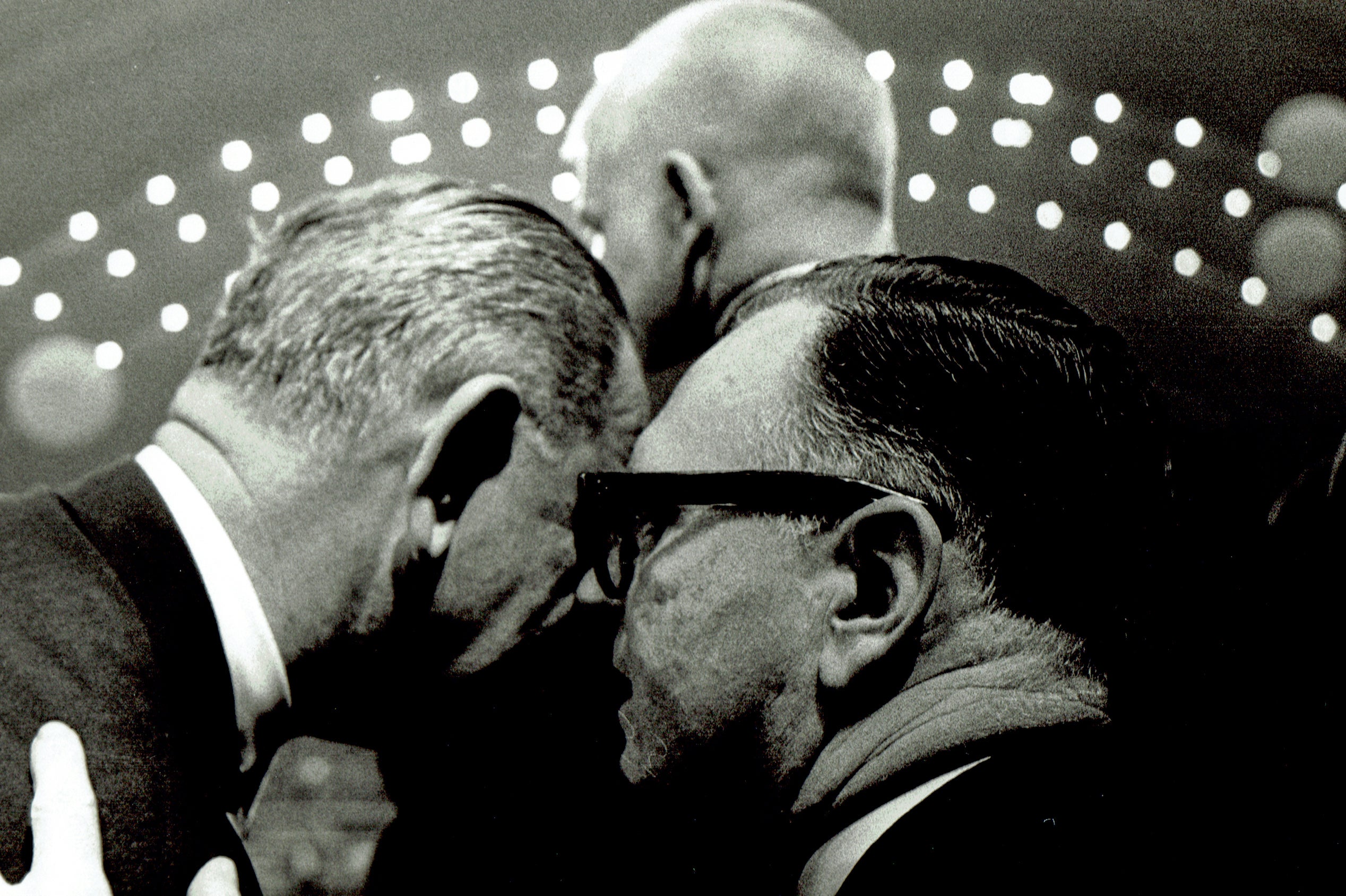 Two men speaking with their heads leaned close together.