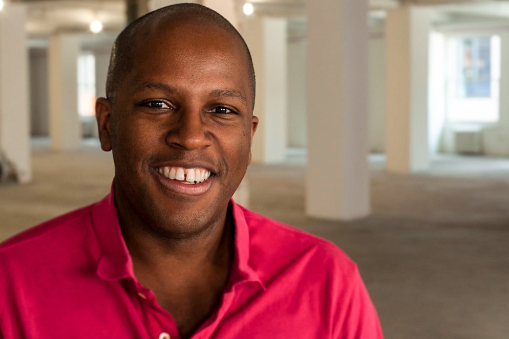 A smiling young Black man wearing a bright pink shirt.