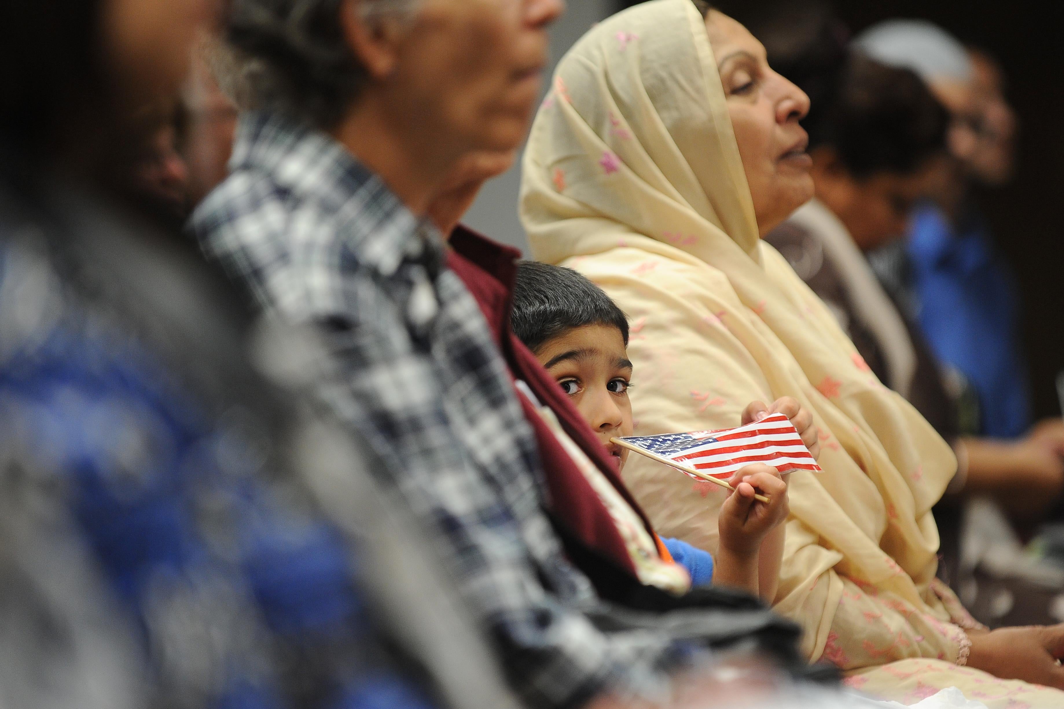 A boy sitting in the audience holds a small American flag next to an older woman wearing a headscarf