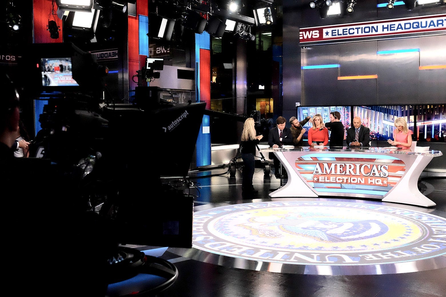 Anchors and staffers prepare around a desk that is emblazoned with a sign that reads "America's Election HQ."
