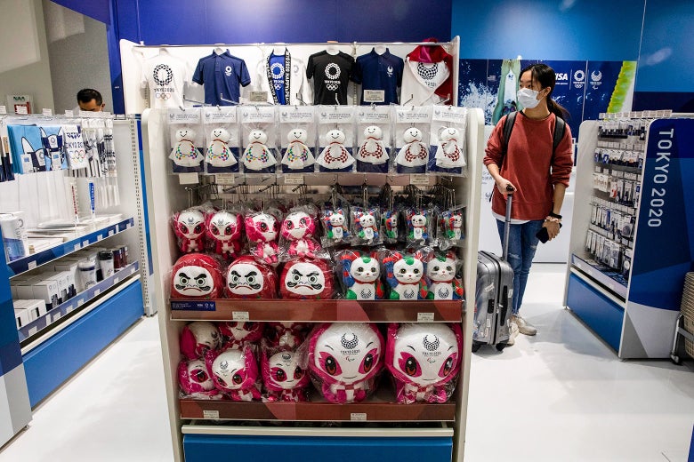 A traveler wearing a surgical mask walks by shelves full of Olympics souvenirs