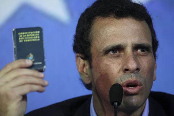 Opposition leader Henrique Capriles holds up a miniature copy of Venezuela's Constitution as he speaks during a press conference in Caracas, Venezuela, March 8, 2013. 