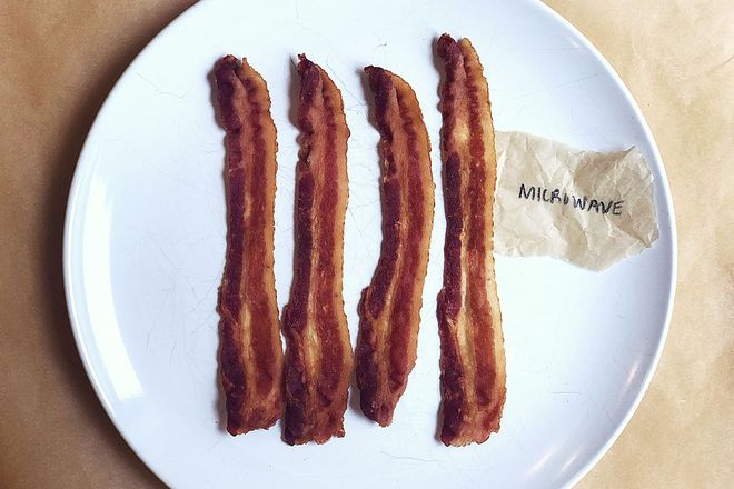 Bacon on a plate with a label: Microwave. The strips are straight and rigid with notable stripes of white fat.