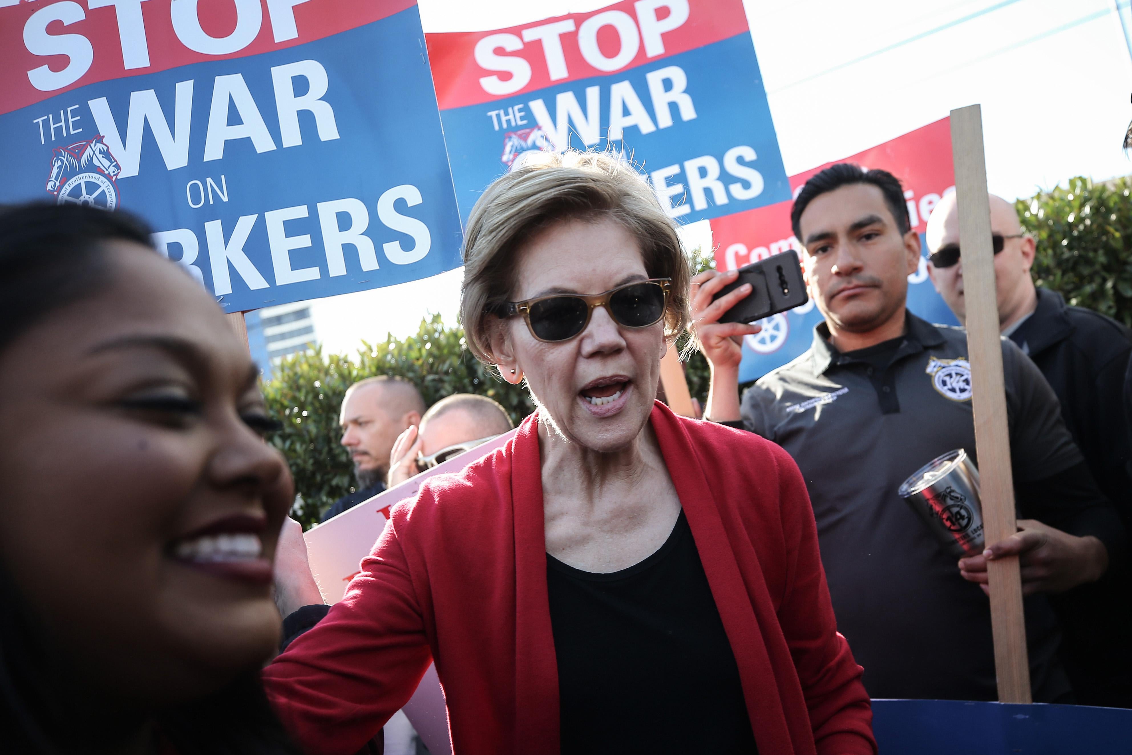 Sen. Warren in sunglasses marching, chanting, and carrying a picket.
