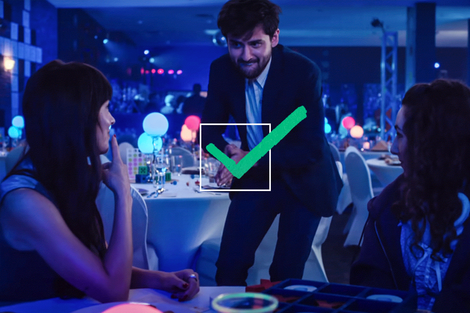 A man approaches a table at a bar mitzvah in a still from the movie. There is a green animated checkmark in a box over the image.