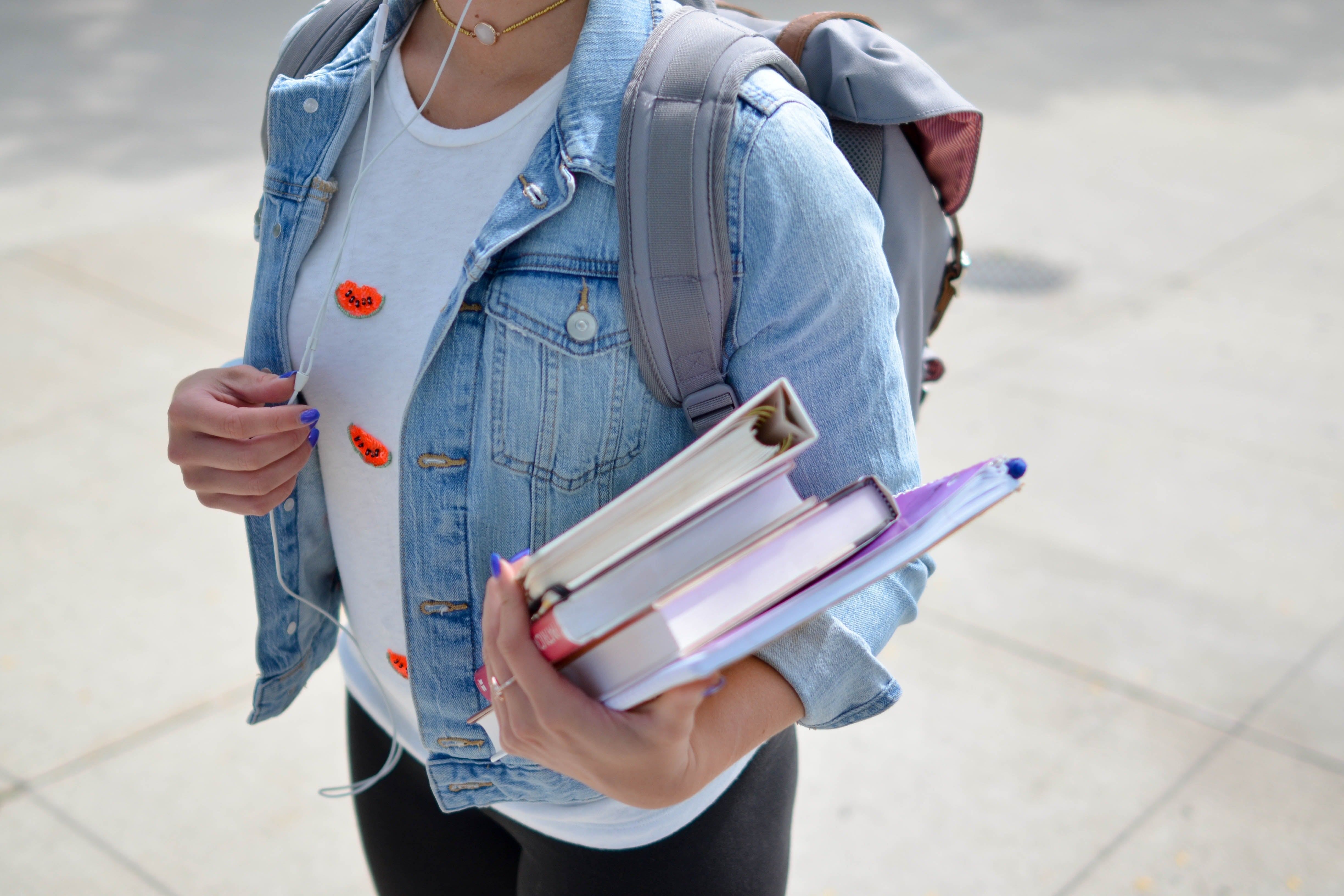 The torso of a woman wearing a backpack and holding books