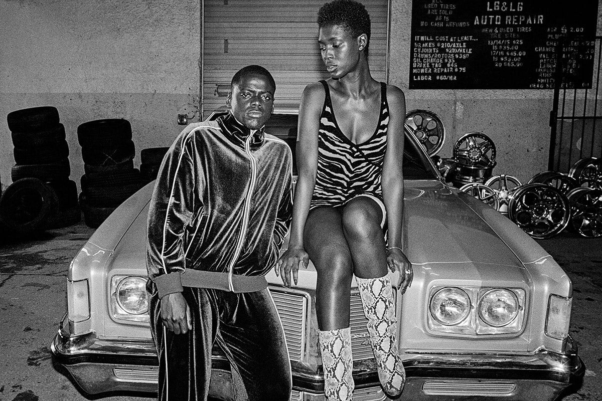 A black-and-white photo of Daniel Kaluuya and Jodie Turner-Smith on the hood of a car.