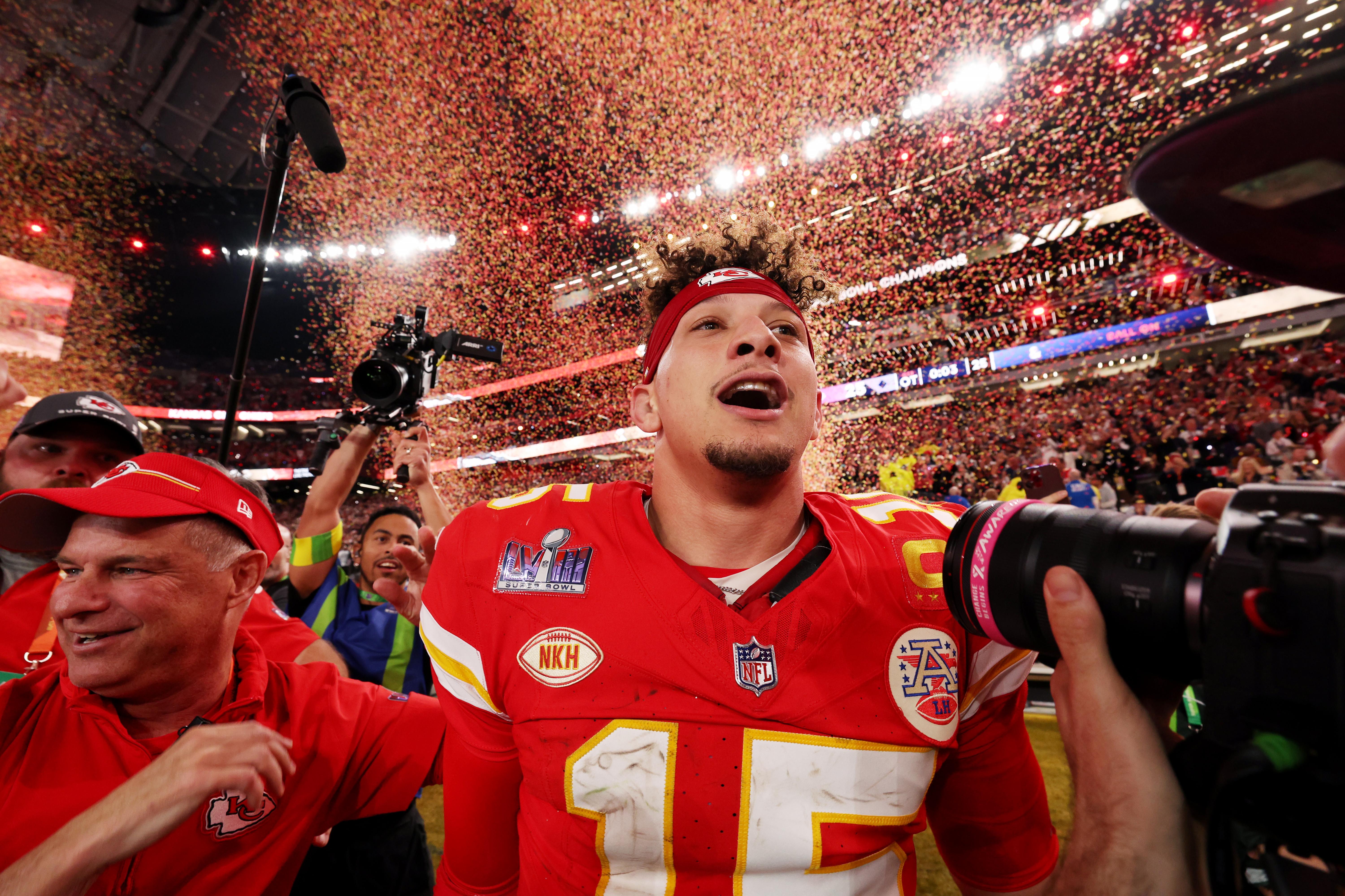Patrick Mahomes gapes as he walks on the field, surrounded by cameras, red and yellow confetti falling behind him.