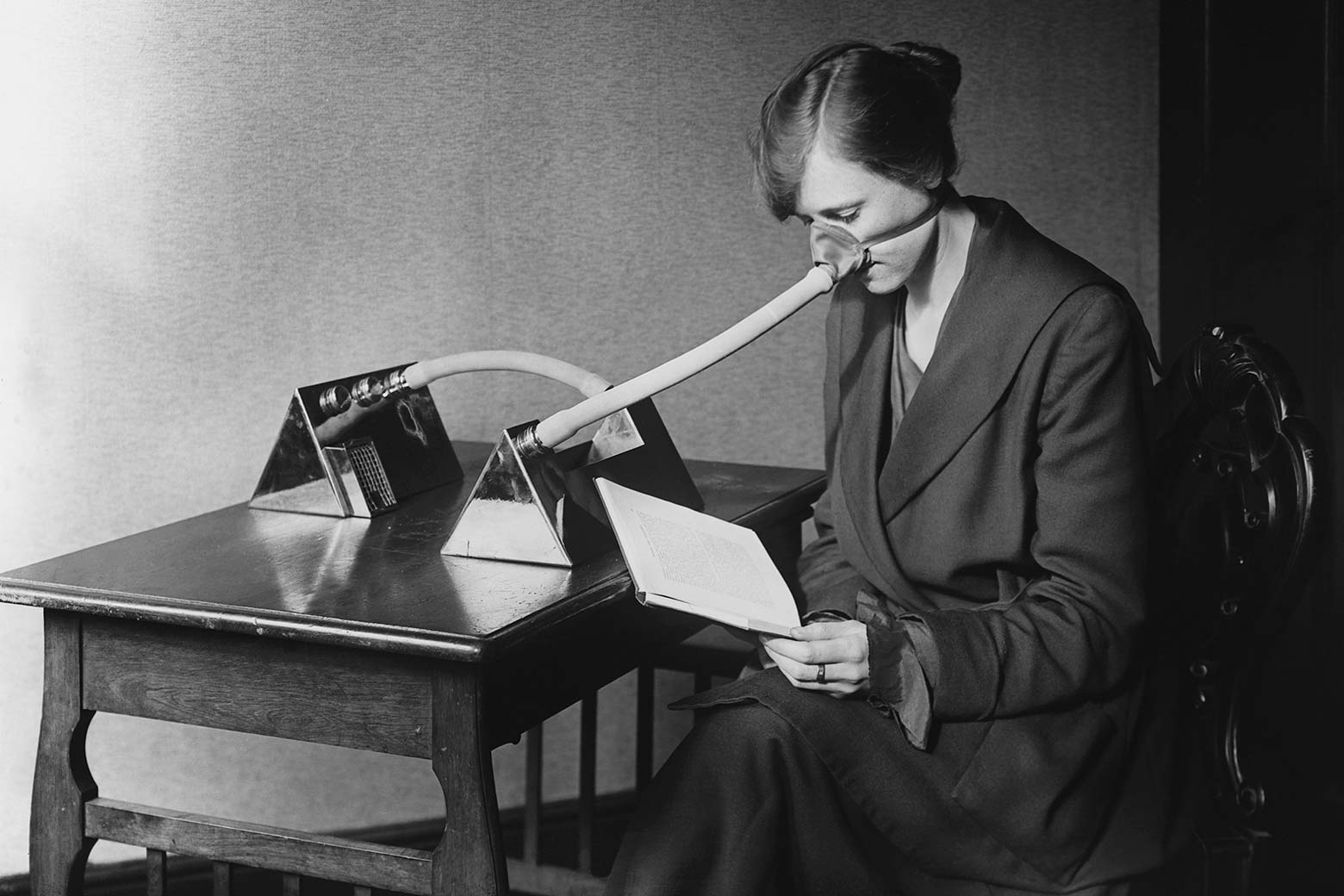 A woman sits at a table wearing a mask over her nose that is connected to a metal device via a series of tubes