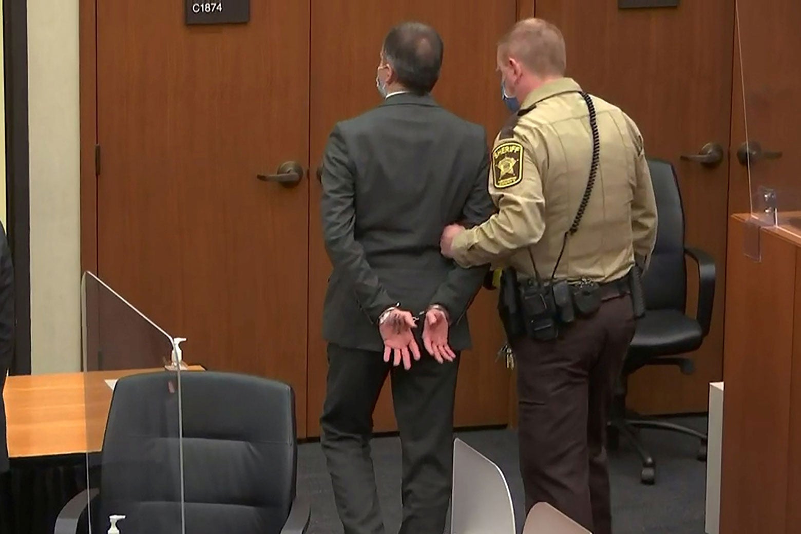 Chauvin being led from courtroom by officer, his hands in handcuffs. 