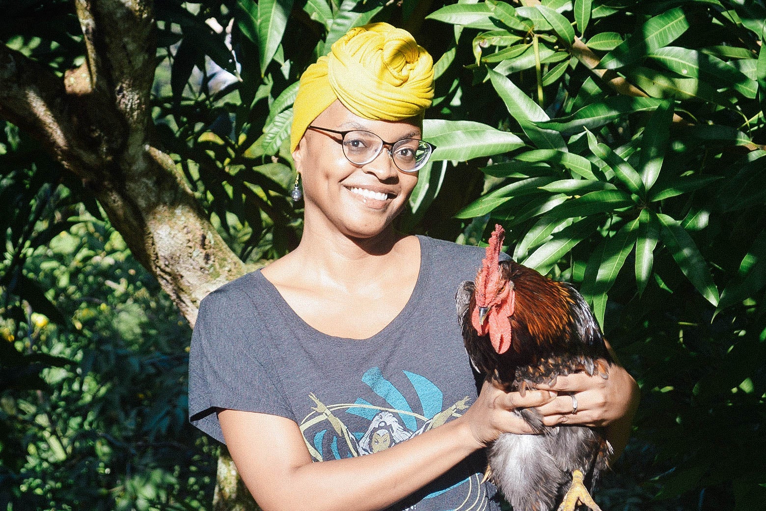 Alyssa Cole in a yellow headwrap and holding a rooster.