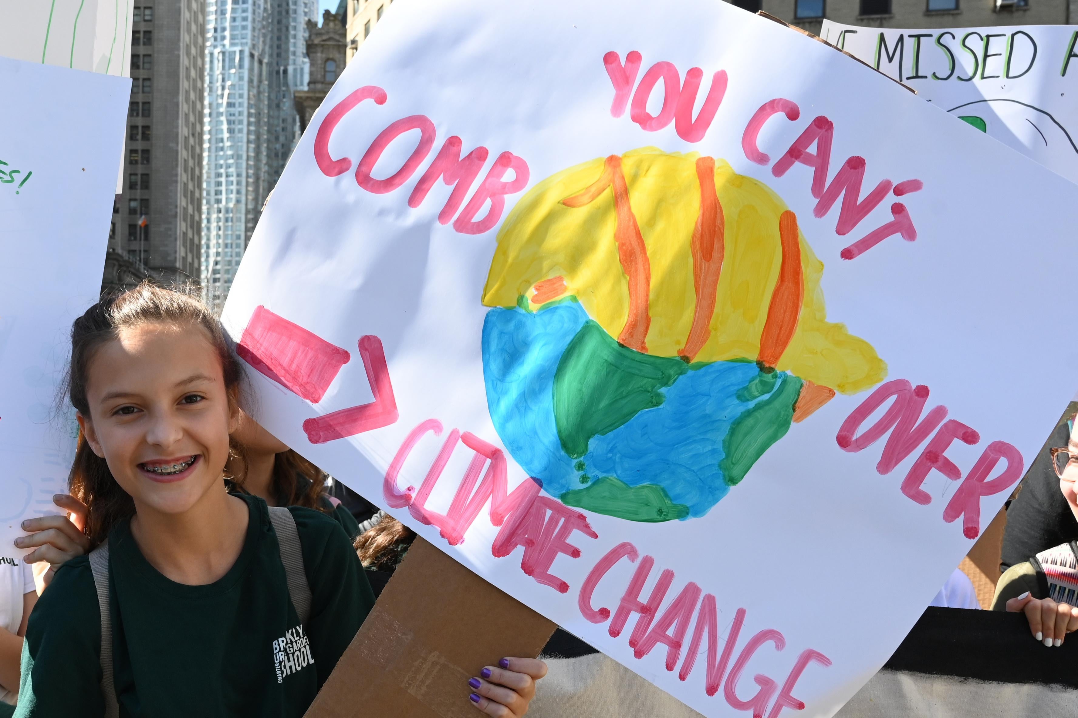 A student holds up a sign that says "you can't comb over climate change."
