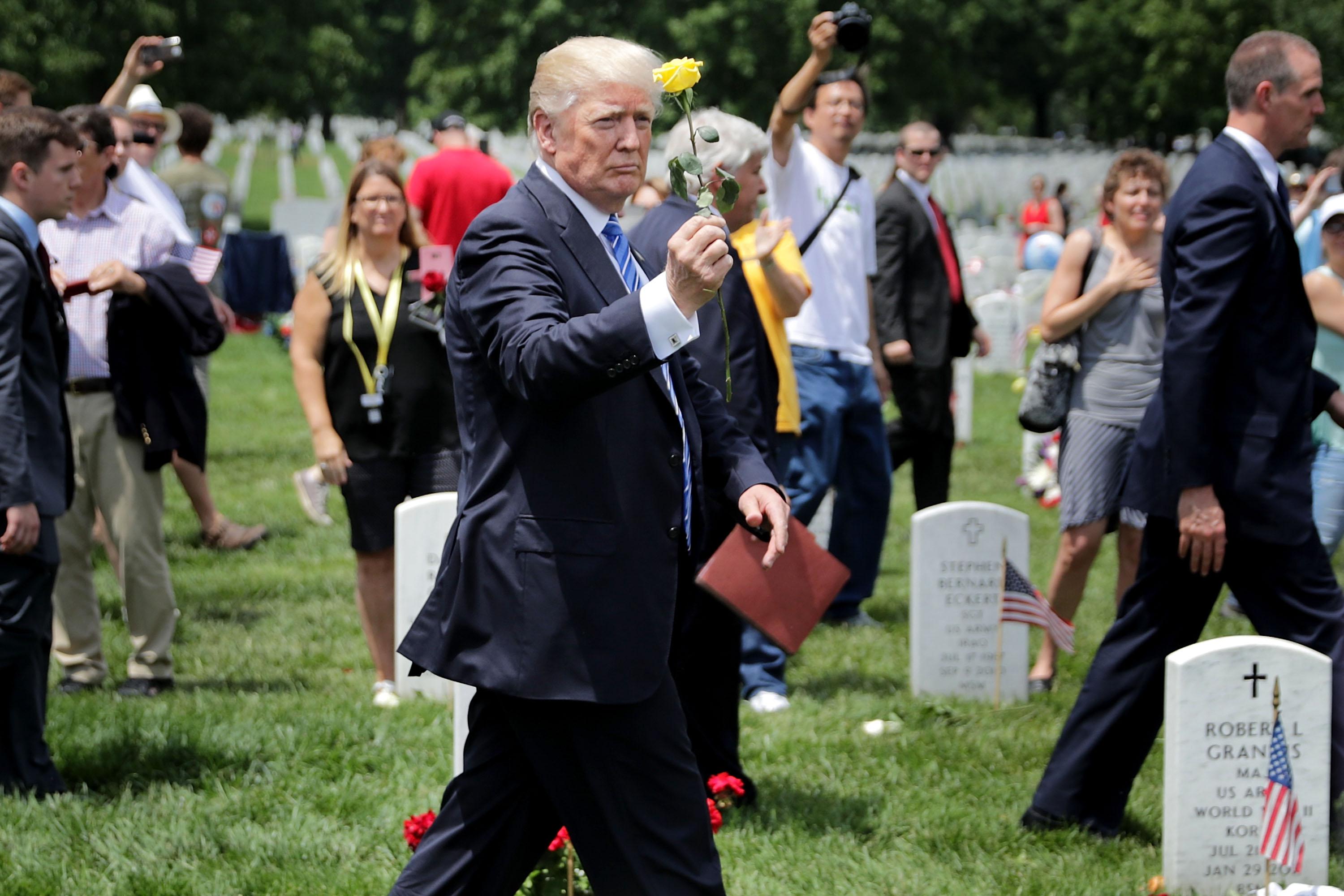 Trump holds up a yellow rose as he walks through the cemetery.