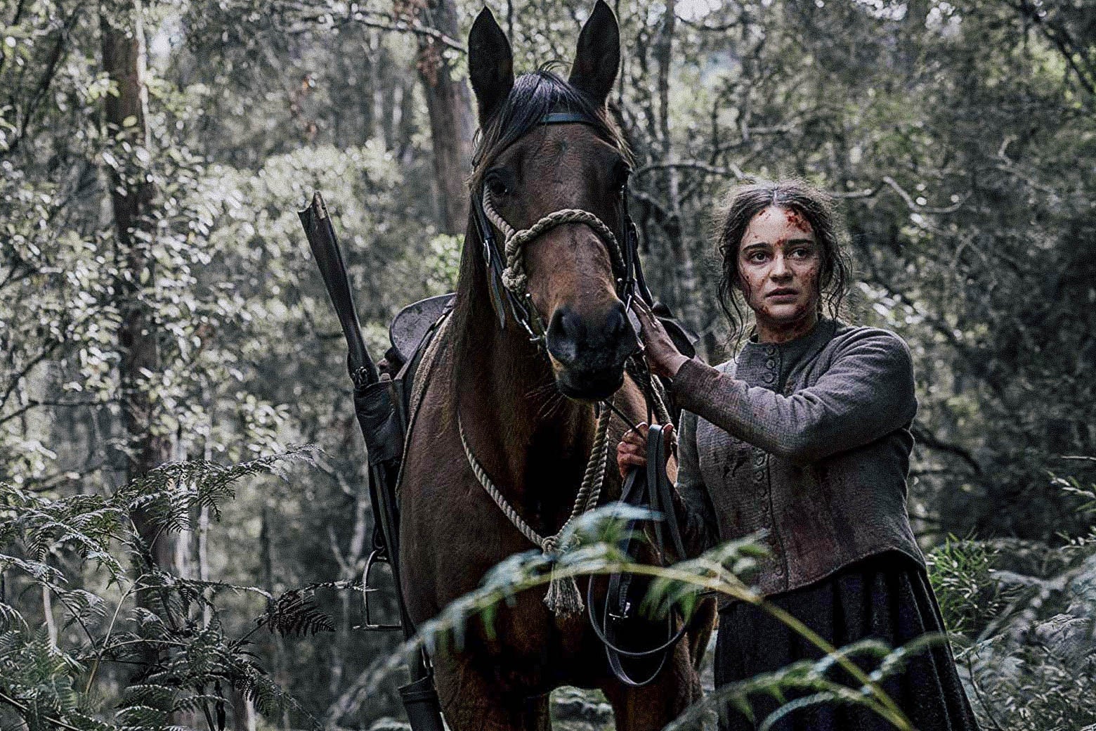 In this still from The Nightingale, a bloodied Aisling Franciosi leads a horse through a forest.
