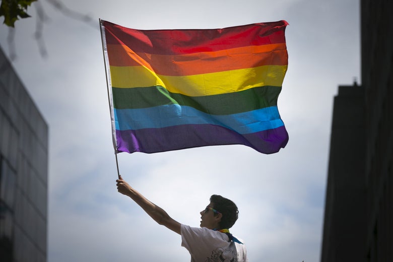 Person waving a rainbow flag on a cloudy day