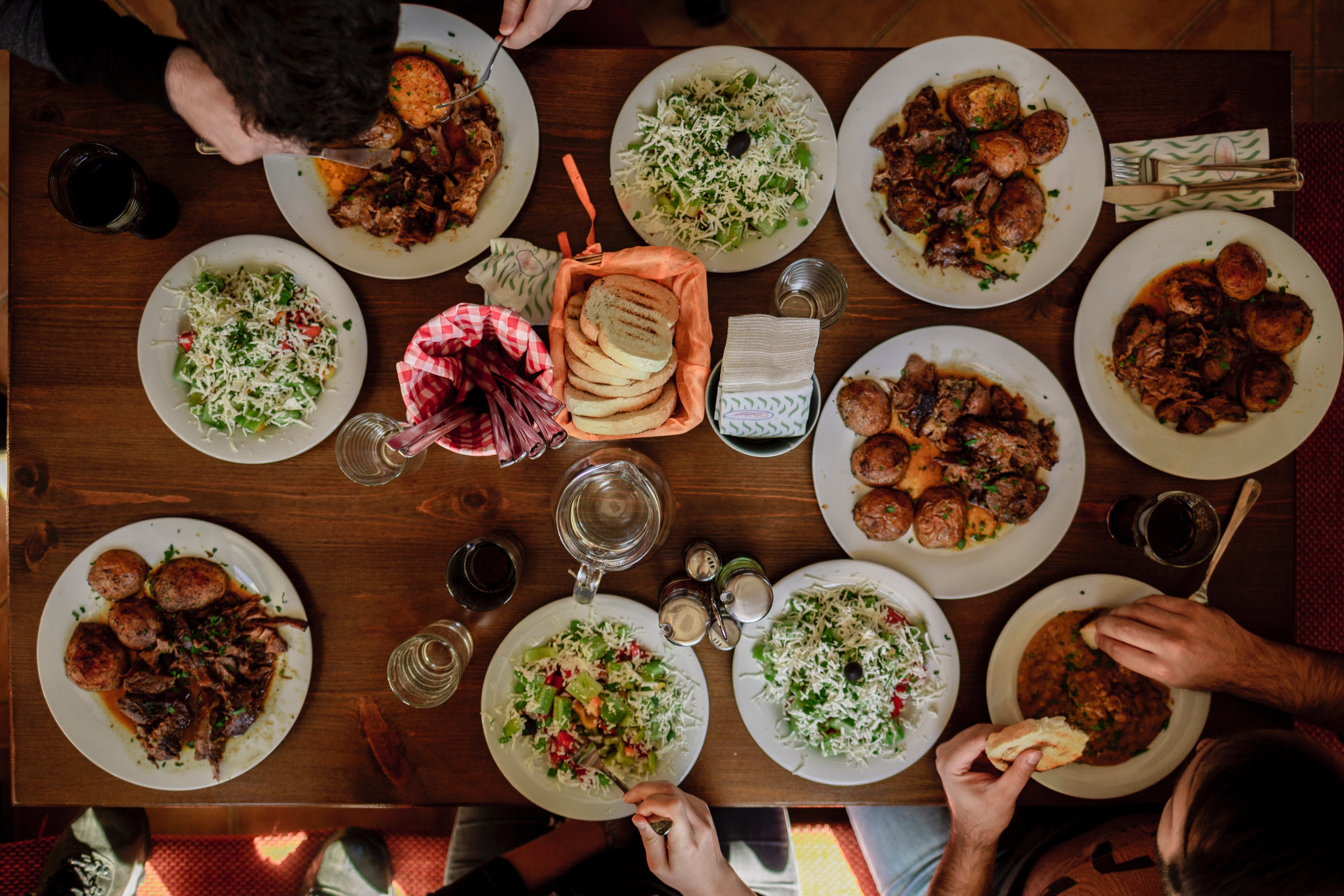 A table full of various dishes is photographed from above. Multiple people enjoy potatoes, salads, and bread in close proximity to one another.