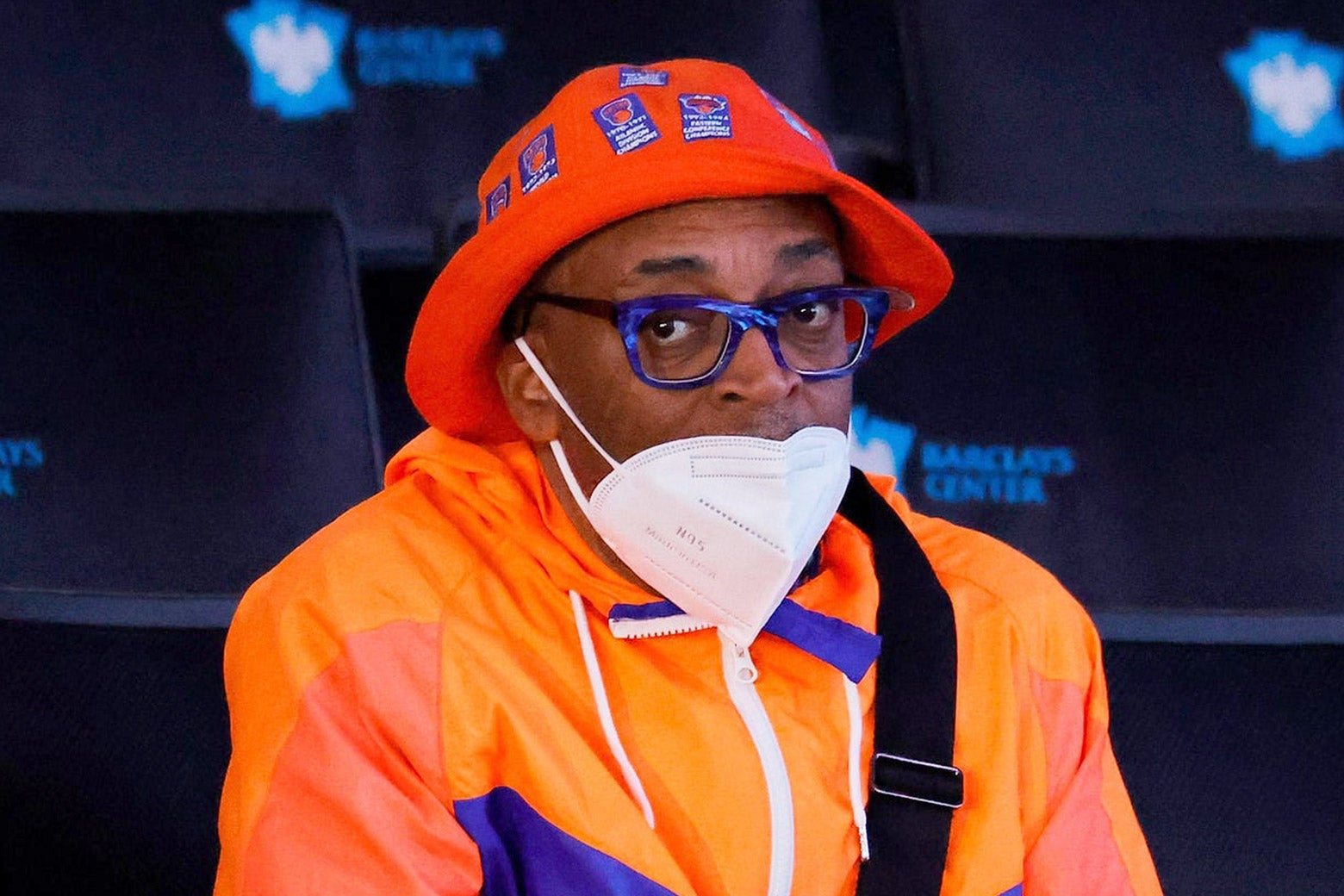 Spike Lee wearing a face mask below his nose and a Knicks hat and rain jacket.