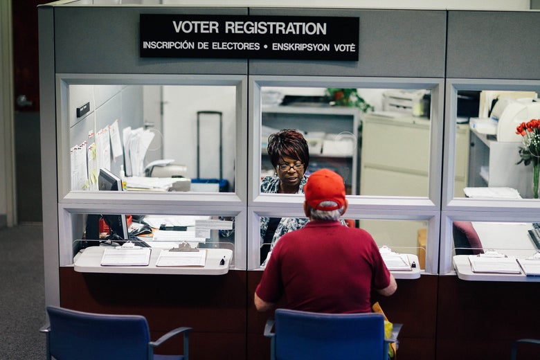 A man sits in front of a voter registration window across from elections worker Dorothy Torrence