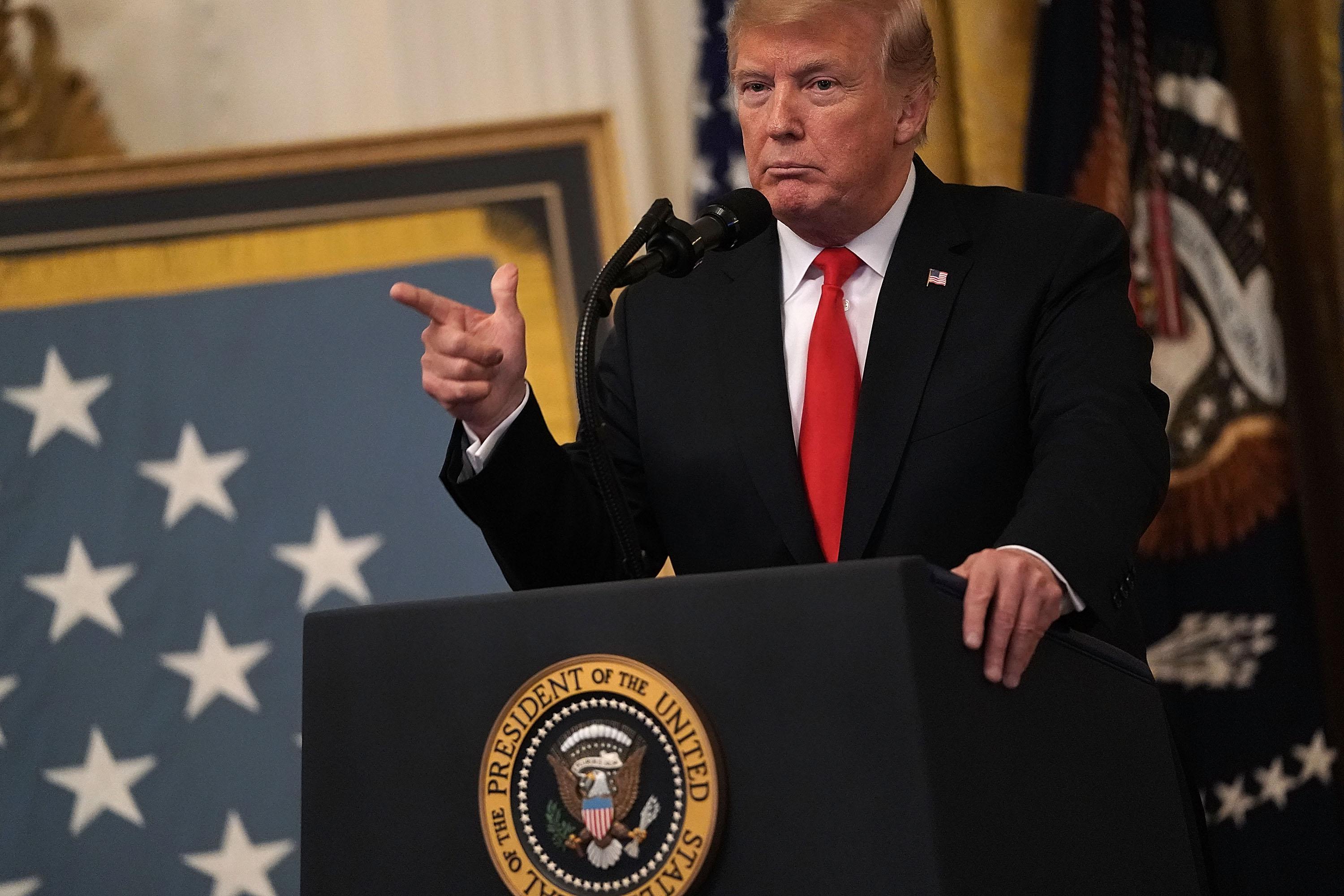 Donald Trump points while standing at a podium in the East Room of the White House