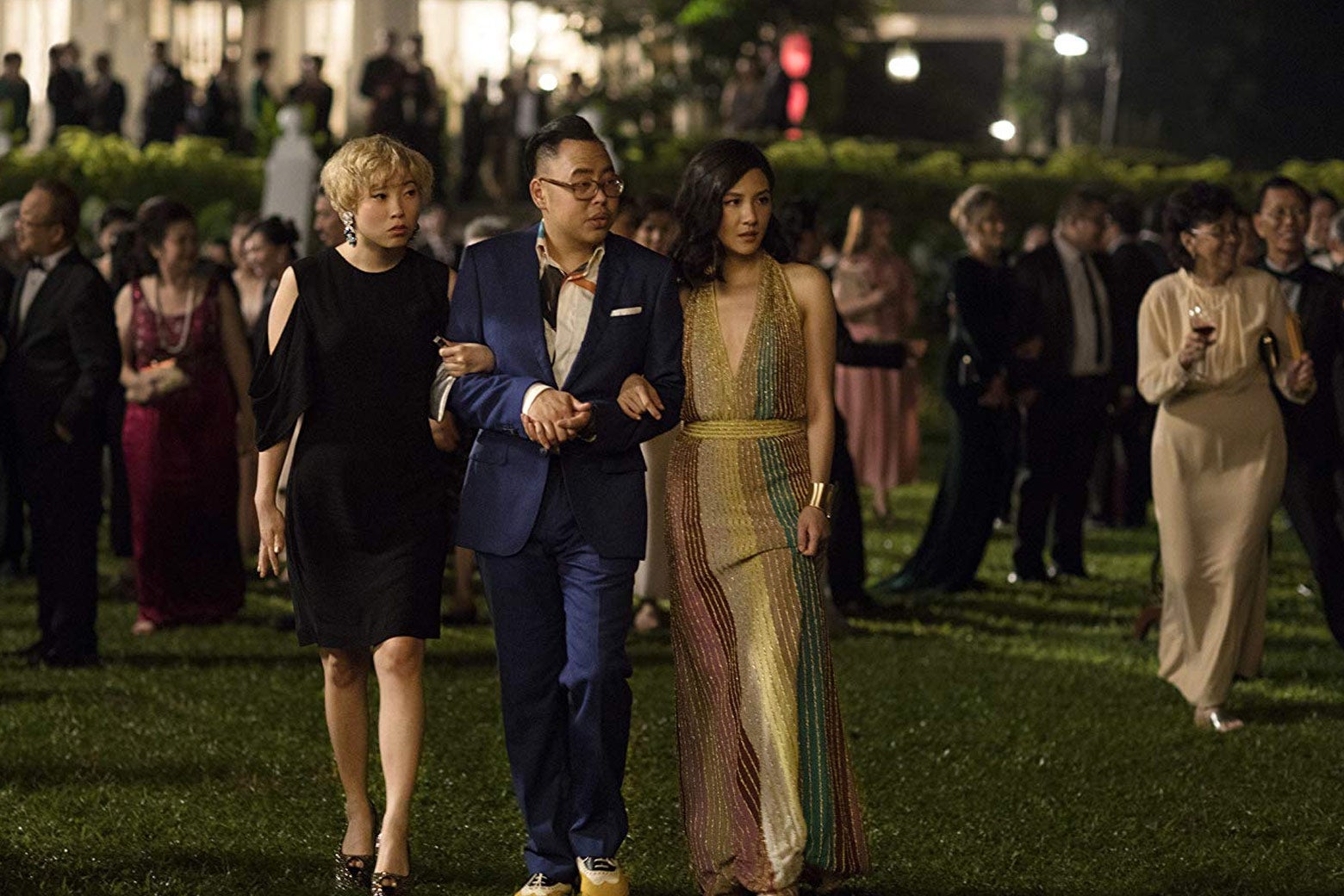 Awkwafina, Nico Santos, and Constance Wu wander the yard of a party in this still from Crazy Rich Asians
