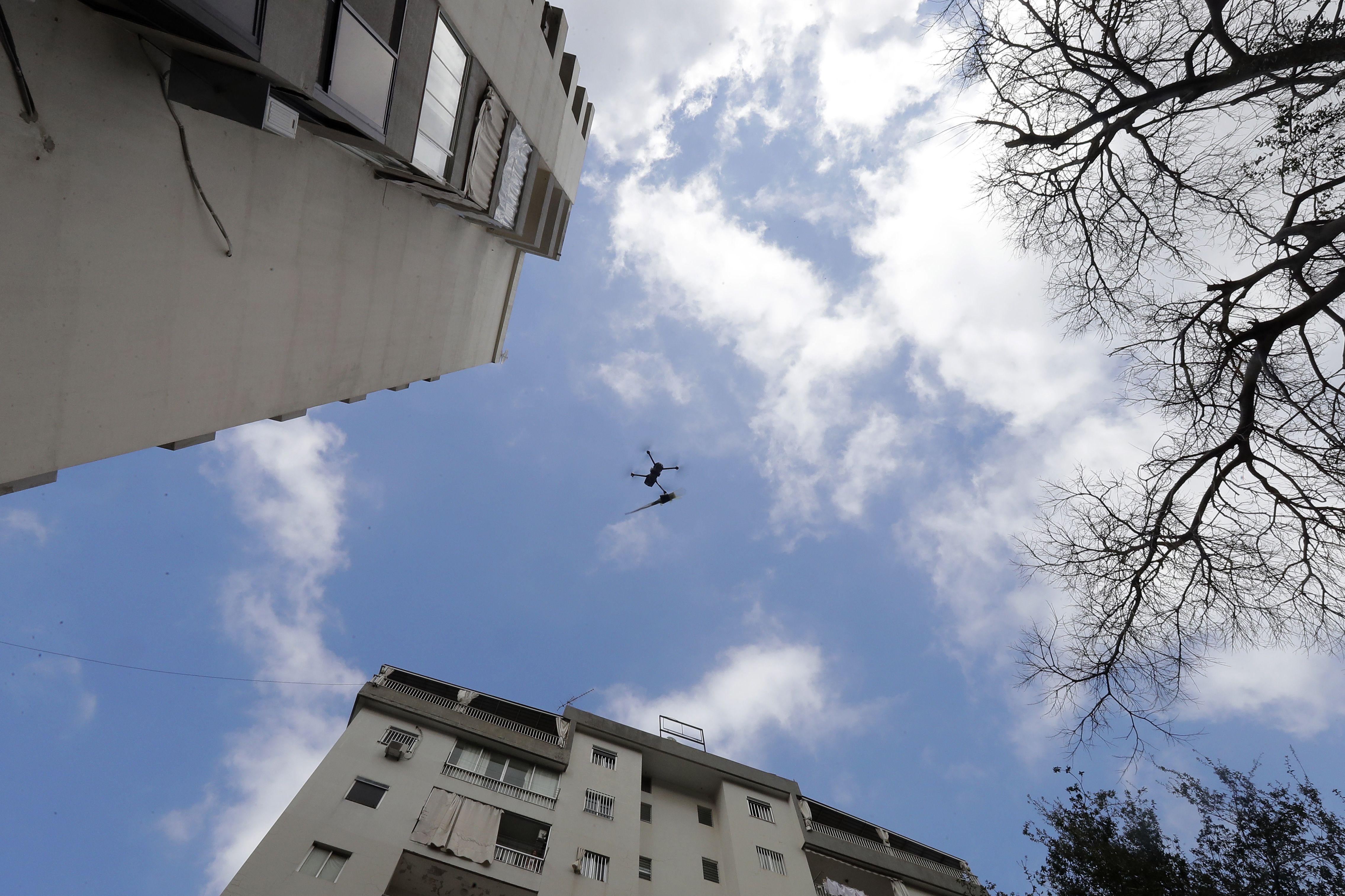 Low-angle shot of a drone flying between tall buildings toward a balcony. There is a rose attached to the drone.