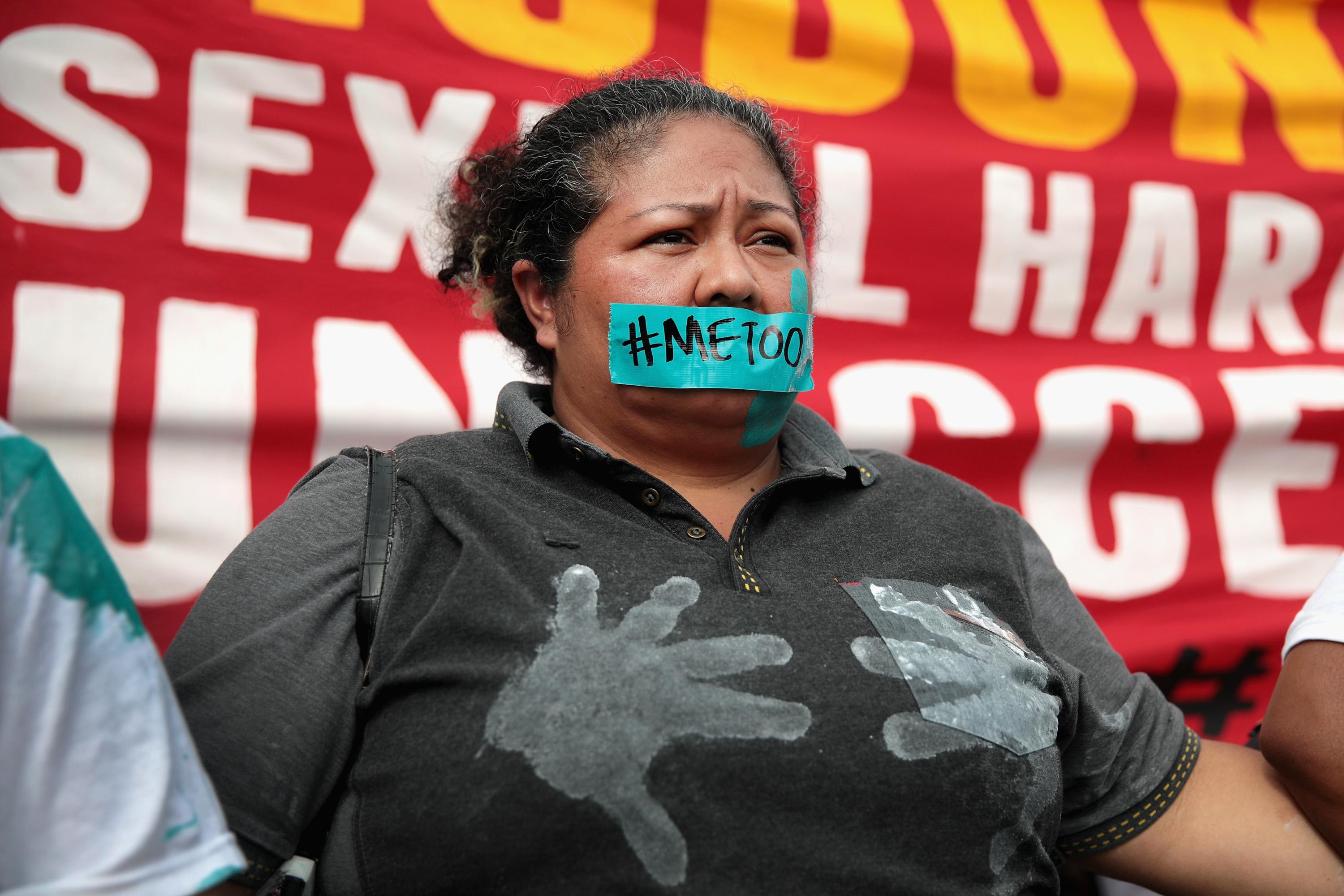 A McDonald's worker stands in front of a protest sign with tape reading "#MeToo" over her mouth.