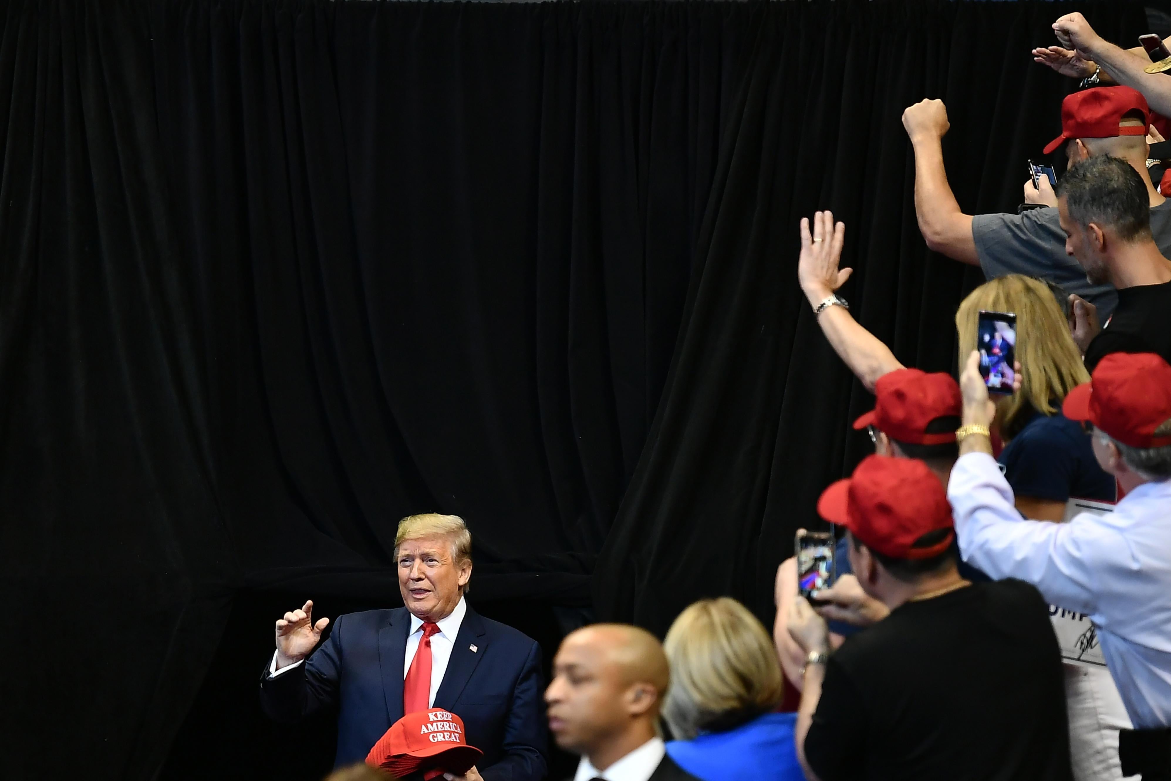 Donald Trump arrives at a rally as supporters in red hats take photos of him and cheer.
