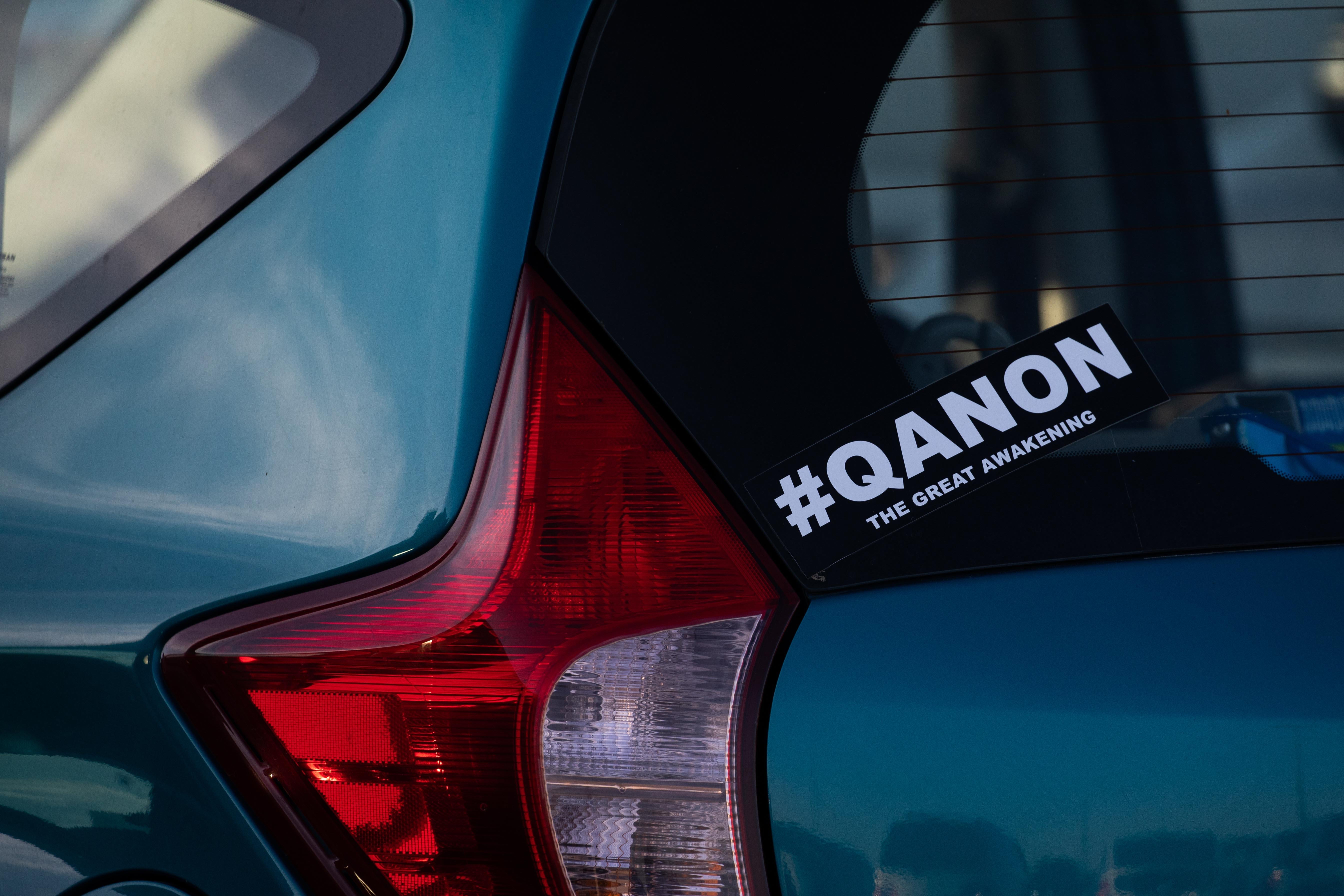A bumber sticker on a car window says #QANON, the great awakening.