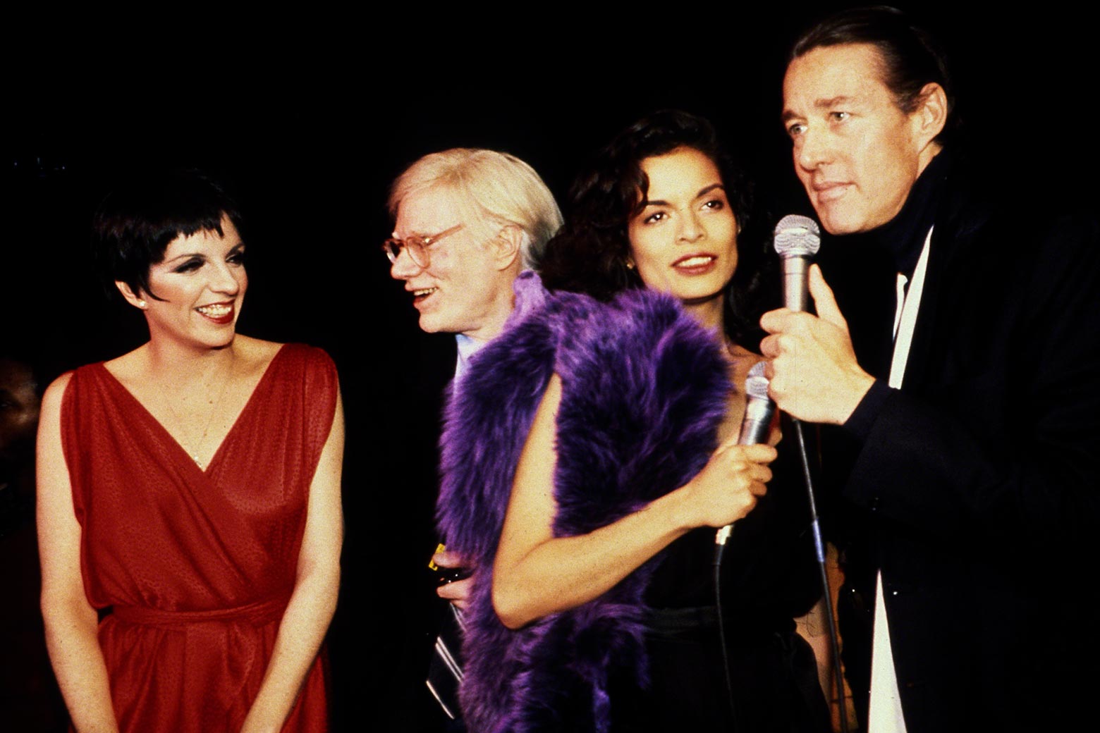 Liza Minnelli, Andy Warhol, Bianca Jagger, and Halston. Halston and Jagger hold microphones.
