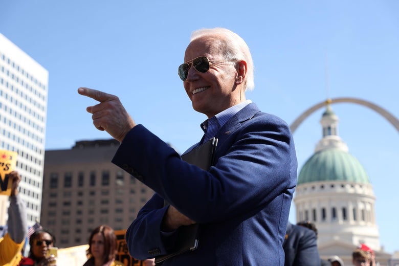 Joe Biden pointing and smiling in front of the Gateway Arch