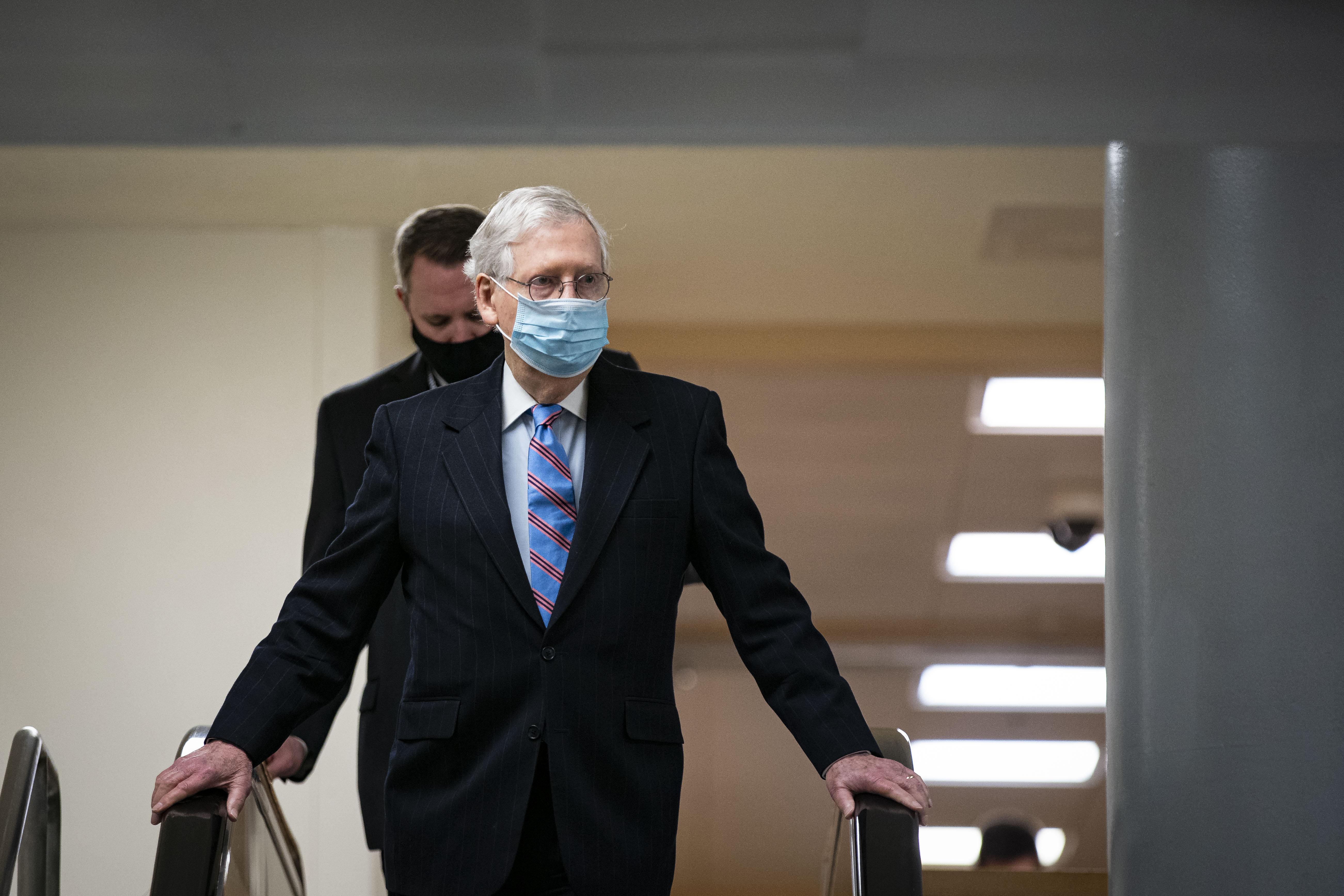 McConnell, wearing a mask, holds the handrails of an escalator down to the subway of the U.S. Capitol