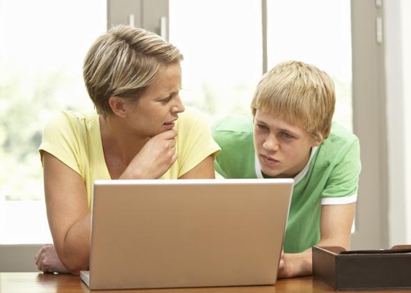 Mother And Teenage Son Using Laptop At Home