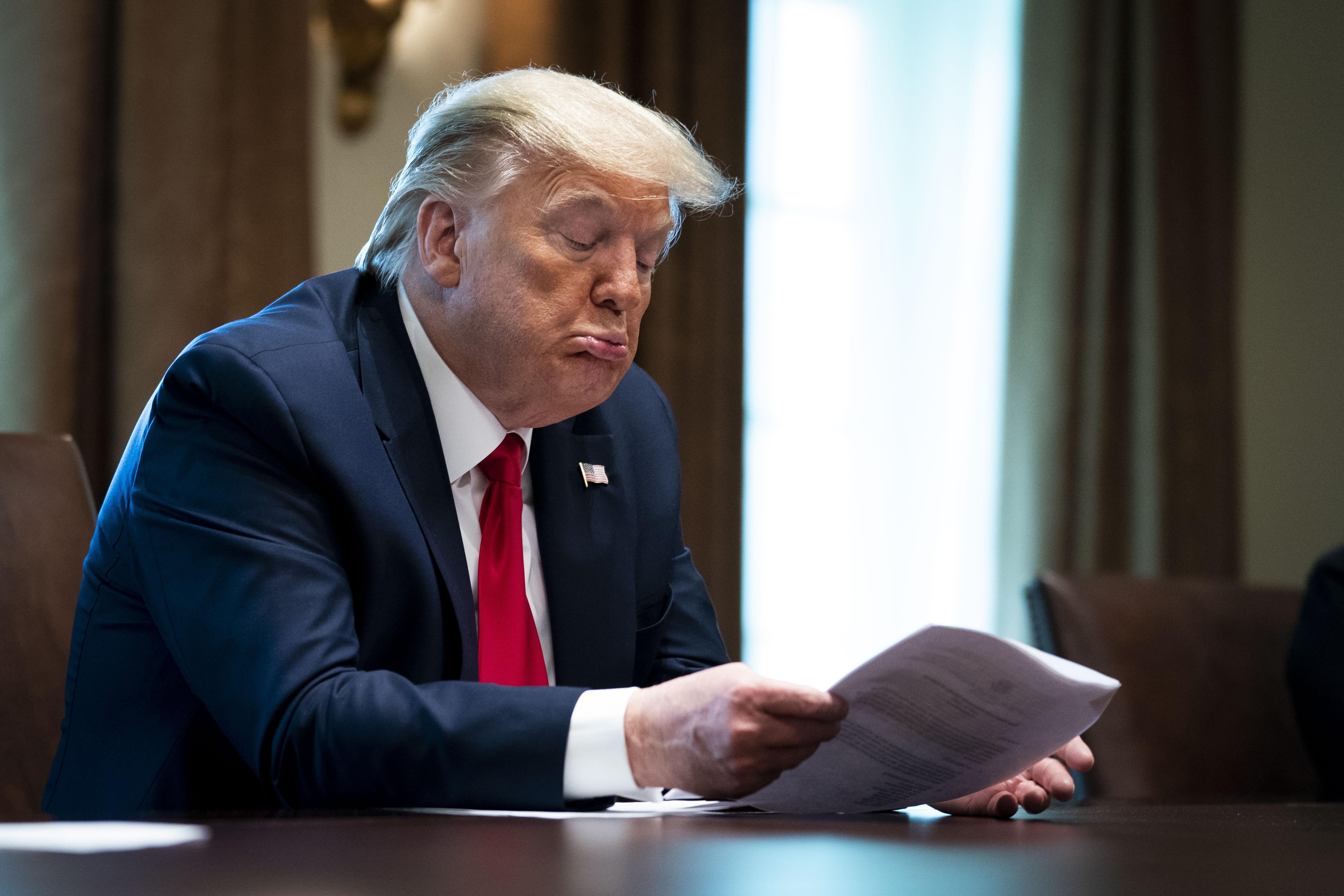 President Donald Trump makes that pursed lips face of his as he looks down at a piece of paper.