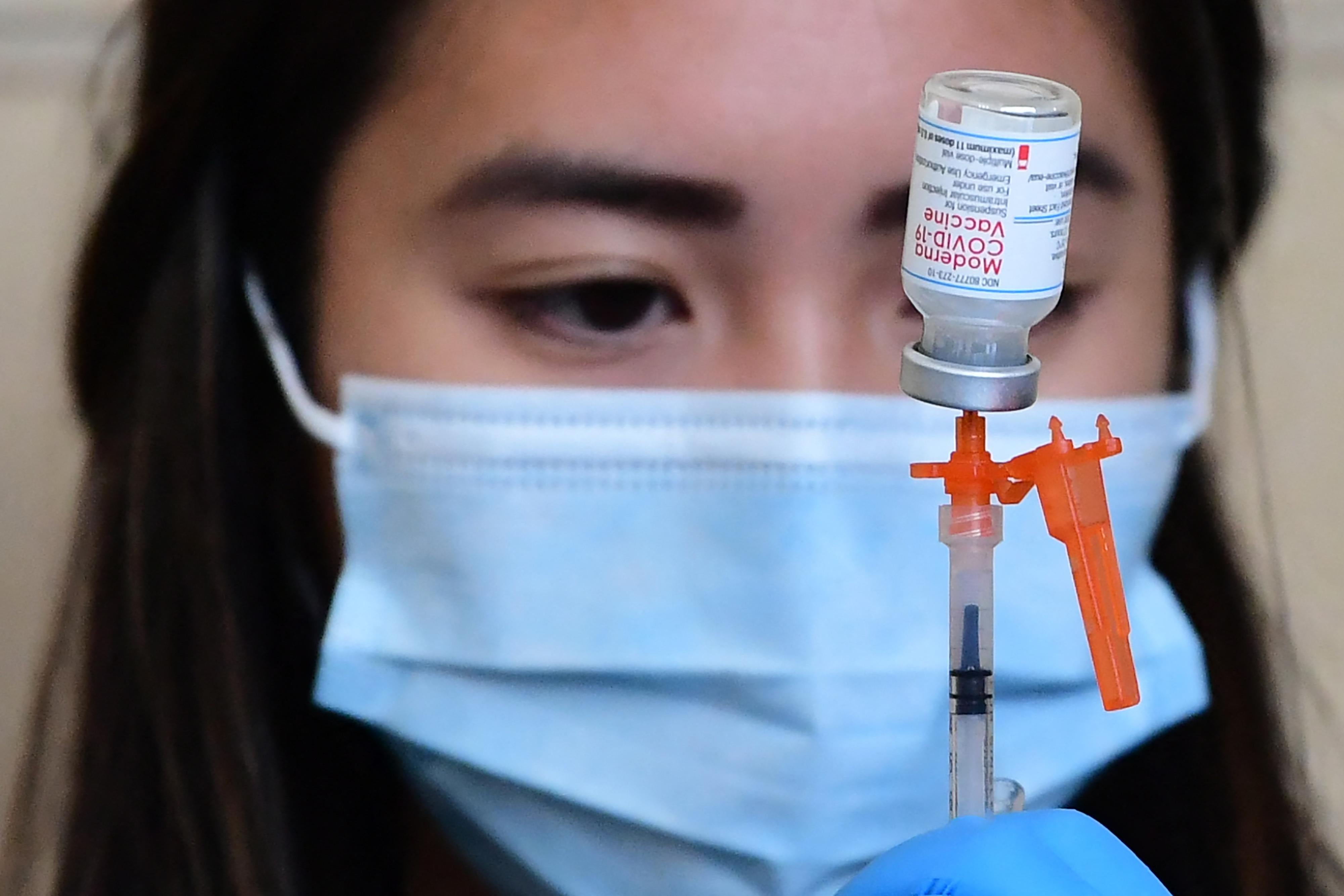 A health worker stares at a vial of the Moderna vaccine as she draws a dose into a syringe