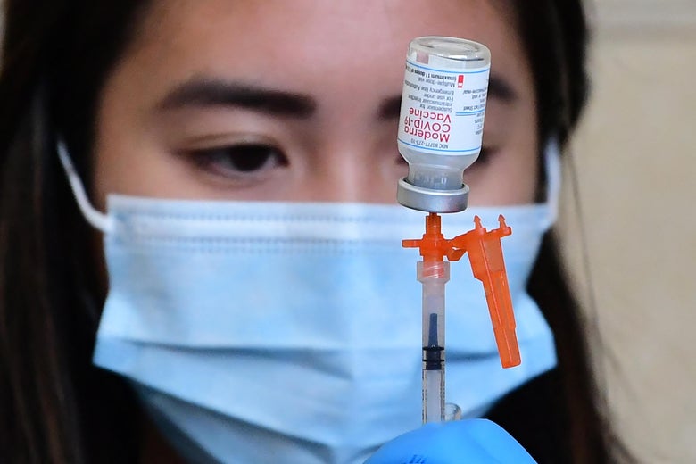 A health worker stares at a vial of the Moderna vaccine as she draws a dose into a syringe