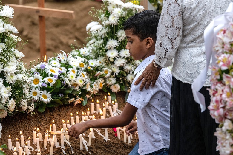 A young boy lights a candle at a grave after a funeral for a person killed in the Easter Sunday attack on St. Sebastian's Church.