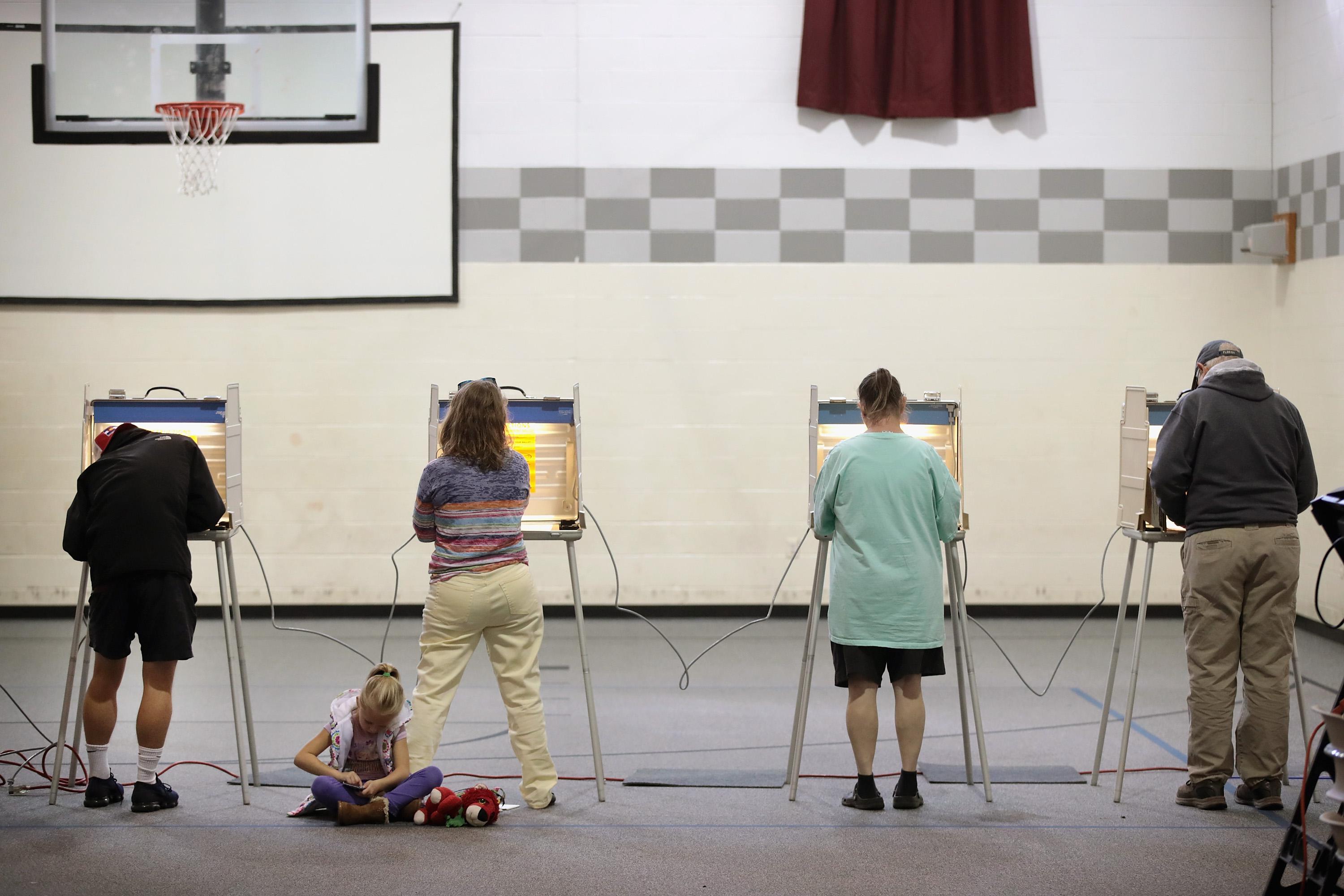 Four people fill out ballots at voting booths in a gymnasium.