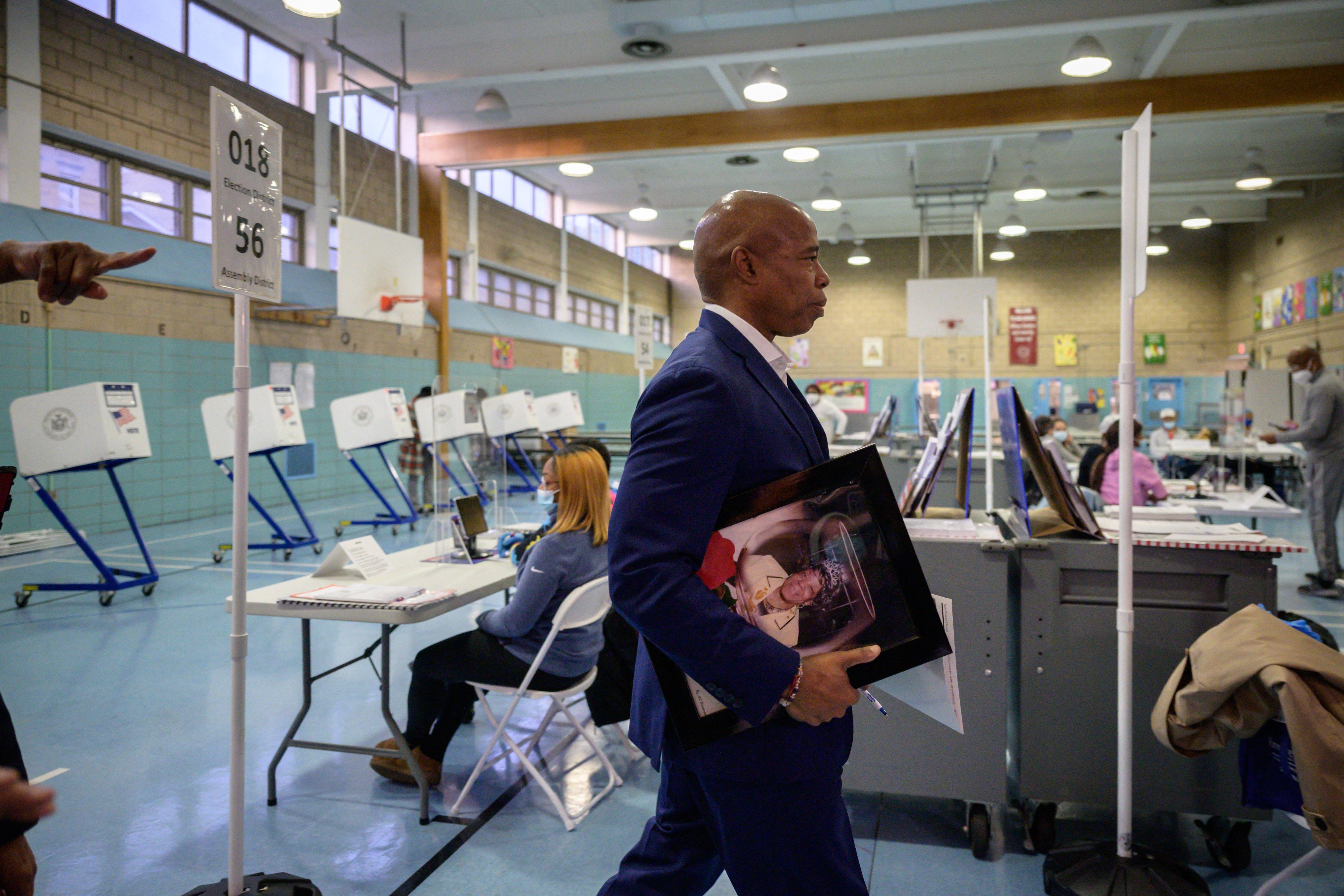 Eric Adams walks into a voting center with a framed portrait of his mother.