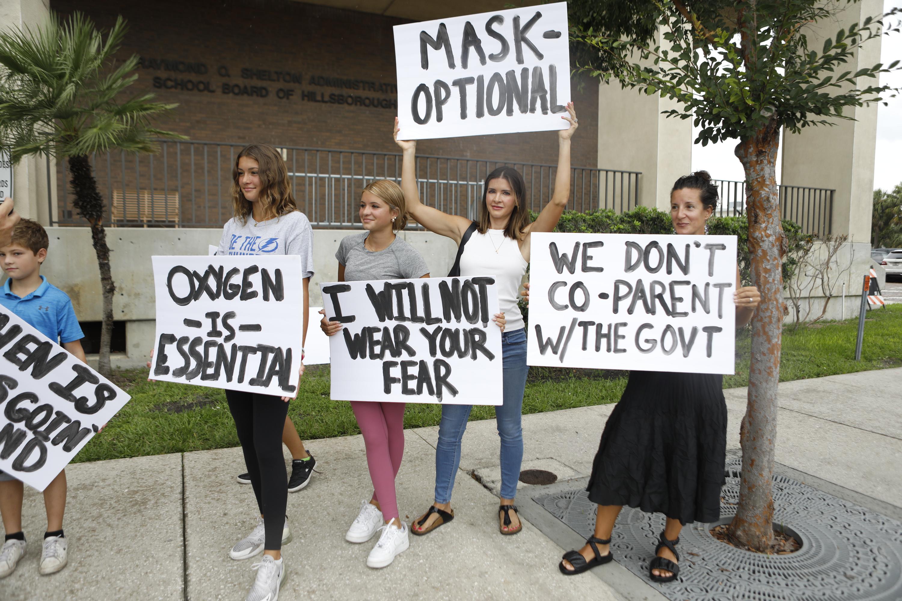 Families hold sign saying things like, "Oxygen is essential" and "I will not wear your fear."